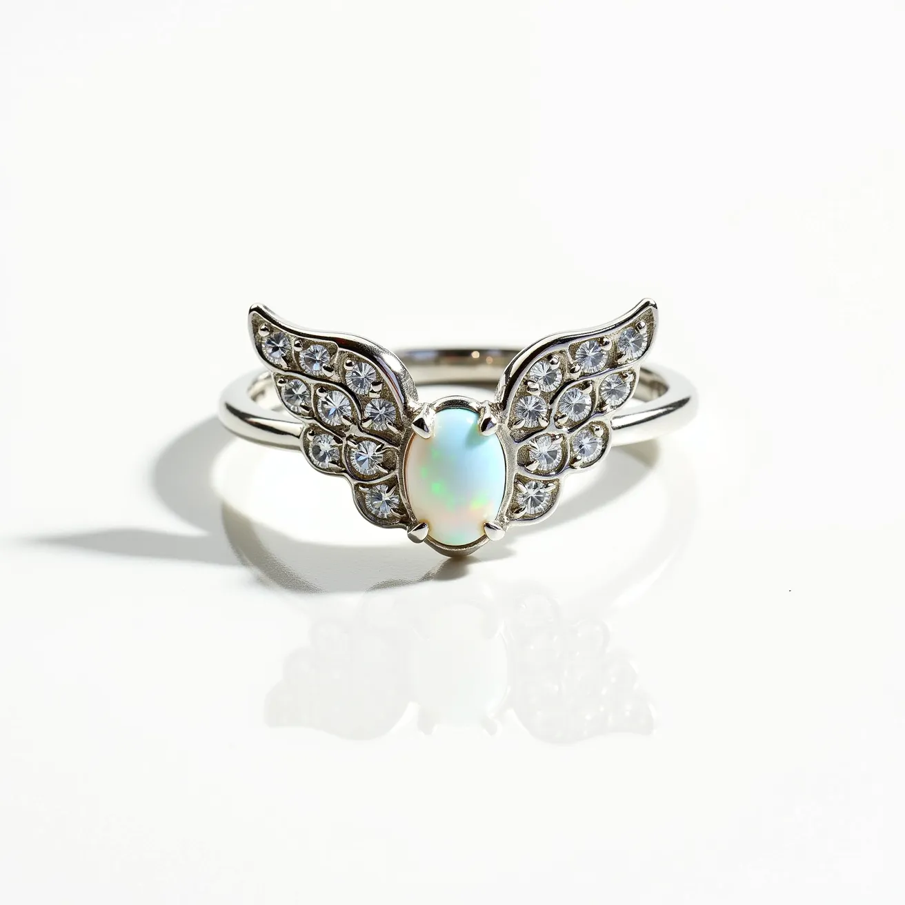 This angel ring features a delicate design with an opal gemstone positioned at the center. The opal, with its oval cut, exhibits a mesmerizing play of colors characteristic of this stone. Flanking the opal are two intricately crafted wings adorned with multiple round-cut clear gemstones, likely set in a pavé style, enhancing the celestial theme. The band appears to be made of polished metal, possibly silver or white gold, complementing the brilliance of the wing's gems. The opal is securely held in place by a prong setting, ensuring stability while accentuating its beauty.