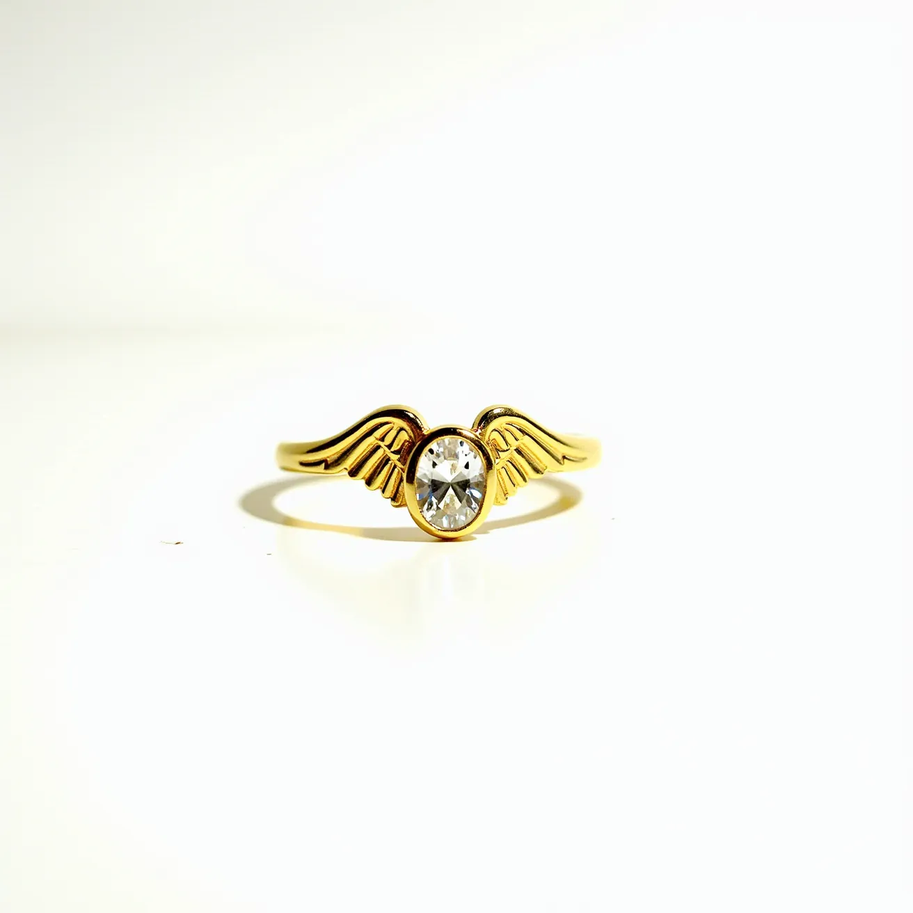 This angel ring features a delicate gold band crafted from what appears to be polished yellow gold. At its center lies an oval-cut clear gemstone, likely a diamond or a high-quality cubic zirconia, securely set in a bezel setting. Flanking the central stone are two intricately designed gold wings, adding a touch of celestial elegance to the piece. The design is seamless, with no visible clasps or attachments, suggesting a simple slip-on style that emphasizes the ring's continuous form and thematic unity.