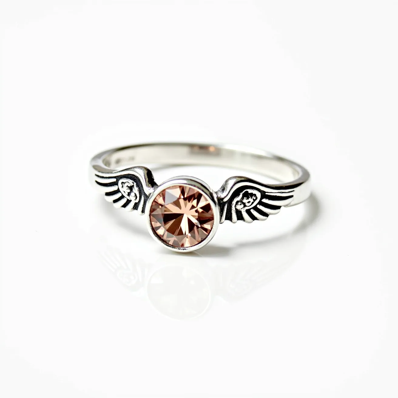 This angel ring features an elegant design with two stylized wings on either side of a prominent central stone. The band appears to be crafted from a silver-toned metal, giving it a sleek and polished appearance. At the center, there is a round-cut gem with a soft champagne hue, securely held in a bezel setting. The wings have delicate engravings, adding an intricate touch to the overall aesthetic. The combination of the angelic motif and the sparkling center stone creates a harmonious and graceful piece of jewelry.