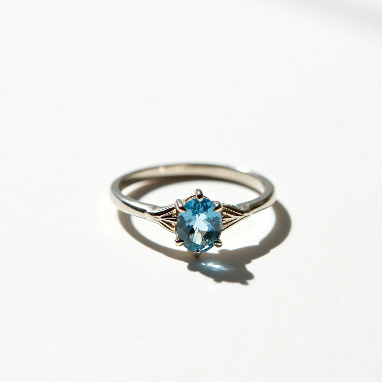 This aquamarine ring features a beautifully cut oval aquamarine gemstone set in a simple yet elegant prong setting, which enhances the stone's brilliance. The band is crafted from a polished metal, likely silver or white gold, providing a sleek and reflective surface that complements the aquamarine's blue hue. Detailed accents on either side of the stone add a touch of sophistication to the design, while the clean and minimal setting allows the gemstone to take center stage. The overall design is both timeless and modern, making it a versatile piece for various occasions.