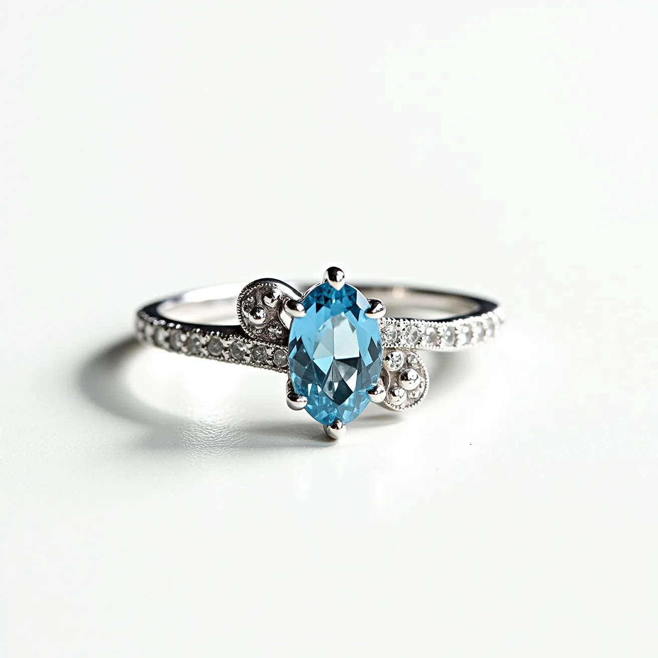 This aquamarine ring showcases an elegant design, featuring a central oval-shaped aquamarine gem, known for its captivating blue hue. The stone is set in a prong setting, allowing maximum visibility and light to pass through, enhancing its natural brilliance. The band of the ring is crafted from a polished precious metal, which could be either white gold or platinum, providing a sleek and sophisticated backdrop. Adorning the band, along each shoulder, is a series of small round cut diamonds set in a pave style, adding sparkle and contrast to the central gemstone. The overall aesthetic is one of timeless elegance, with intricate scrollwork beside the aquamarine, which adds a touch of vintage charm to the piece.