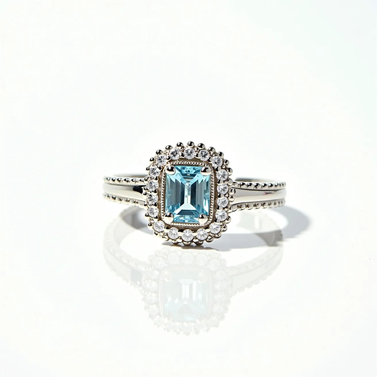 This aquamarine ring features a central, emerald-cut aquamarine gemstone that is set in a prong setting, allowing the captivating blue-green hues of the stone to be prominently displayed. Surrounding the aquamarine is a halo of smaller round-cut diamonds, which add a sparkling contrast to the centerpiece. The band of the ring is crafted from polished white metal, possibly white gold or platinum, and includes intricate detailing with a row of small round embellishments along the sides, enhancing its elegance. The ring’s design incorporates a delicate balance of sophistication and brilliance, making it a striking piece of jewelry.