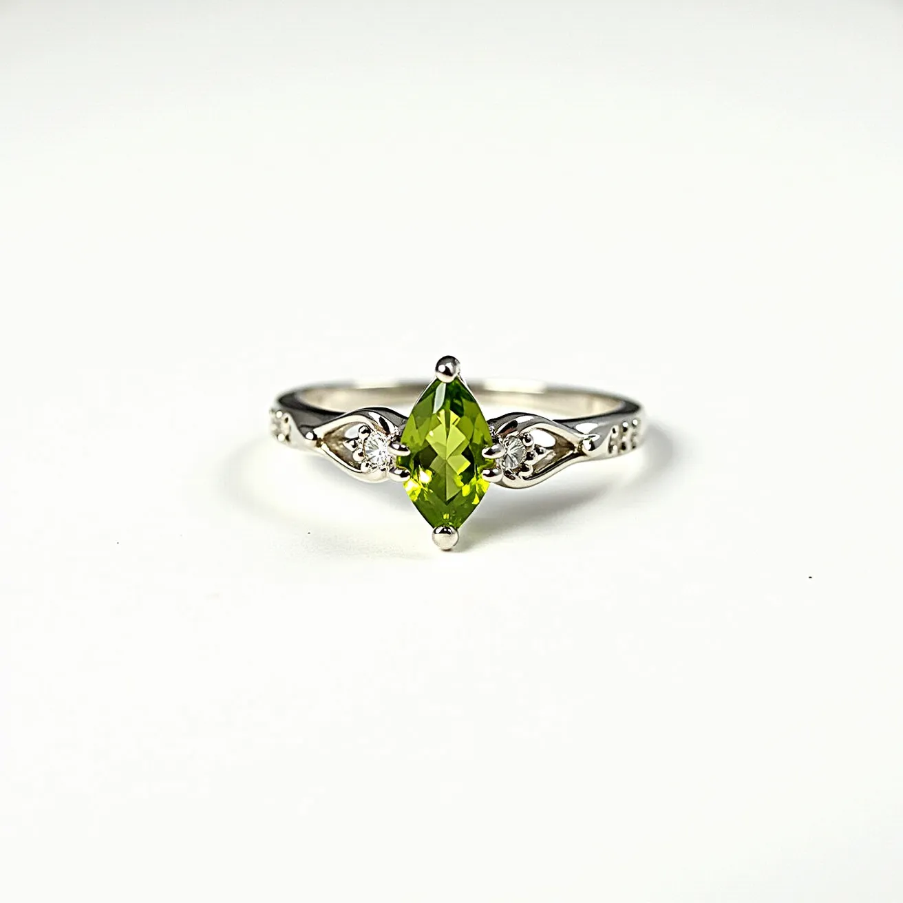 This august birthstone ring features a marquise-cut peridot, the traditional gemstone for August, prominently set in a four-prong setting. The lively green hue of the peridot is complemented by the band, which appears to be made of a polished silver or white gold material. On either side of the central peridot are small, round white stones, likely diamonds or cubic zirconia, set in intricate decorative settings that enhance the ring's elegance. The band itself is adorned with delicate patterns, adding visual interest and sophistication to the piece.