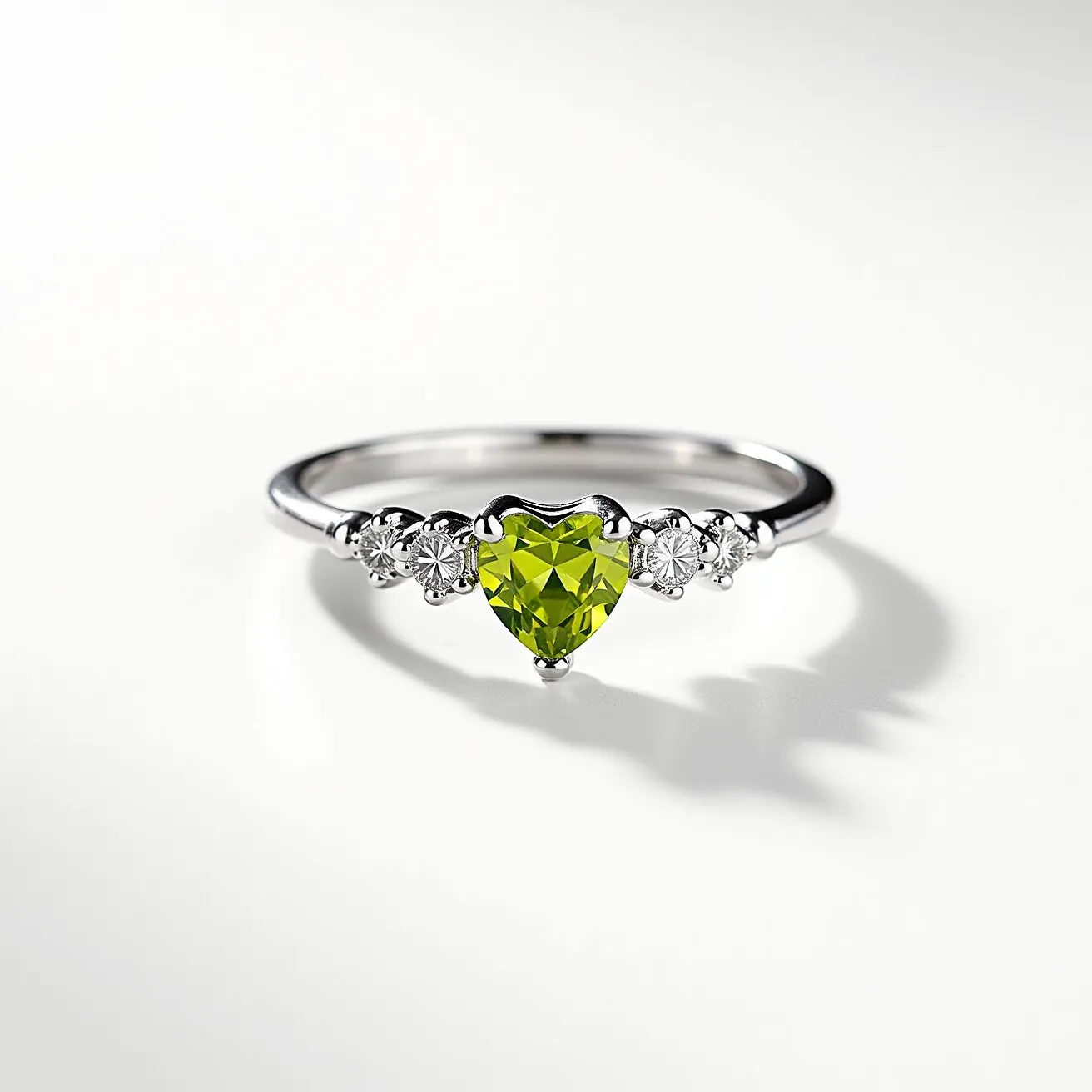 This august birthstone ring features a beautifully cut heart-shaped peridot as its centerpiece, set within a polished metal band that appears to be made of silver or white gold. Flanking the vibrant green peridot are two smaller round-cut white stones on each side, likely diamonds or cubic zirconia, adding an elegant contrast to the central stone. The overall setting accentuates the peridot’s color, enhancing its bright and lively appearance, characteristic of an august birthstone. The band is designed with a sleek, simple elegance that complements the sparkle of the gems while ensuring the ring remains comfortable and attractive for everyday wear.