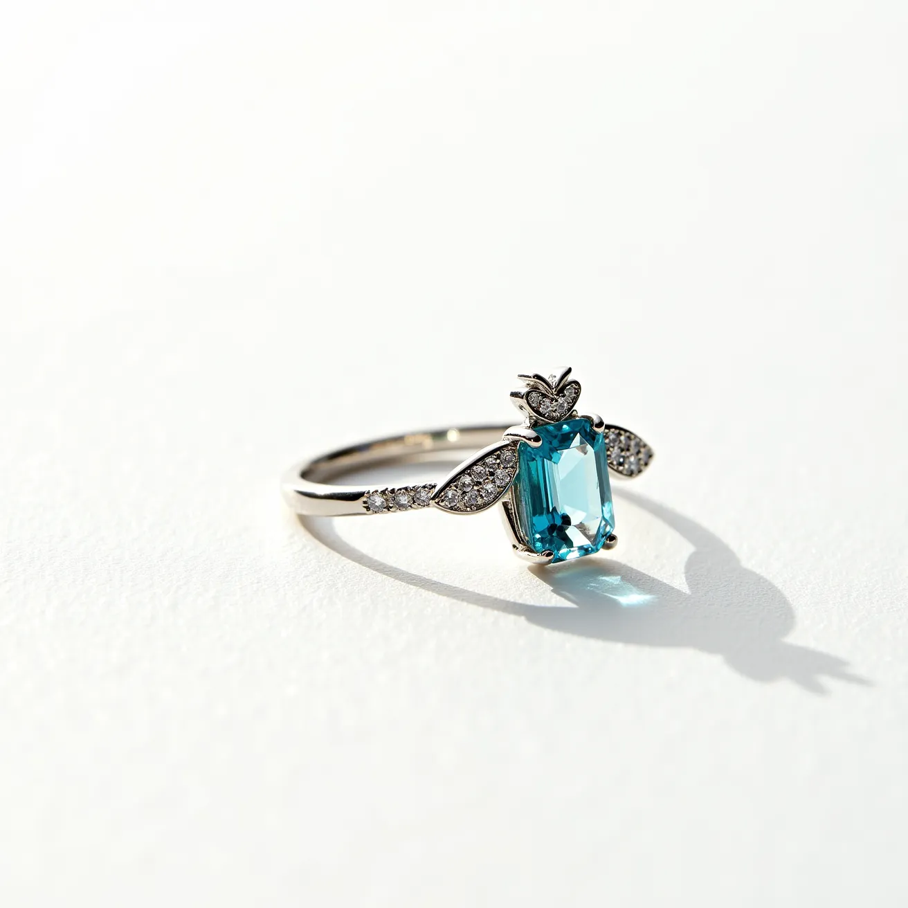 This bee ring features a prominent blue gemstone with an emerald cut, held securely in a prong setting that forms the body of the bee. The wings are adorned with small, sparkling white stones, likely diamonds, set in a pave style, adding an elegant shimmer to the design. The ring band appears to be made from a shiny metal, possibly white gold or platinum, complementing the overall aesthetic of the piece. The bee motif is intricately crafted, showcasing detailed antennae and a charming, delicate design. The ring does not feature any additional clasp or attachment, focusing attention on the bee motif as the centerpiece.