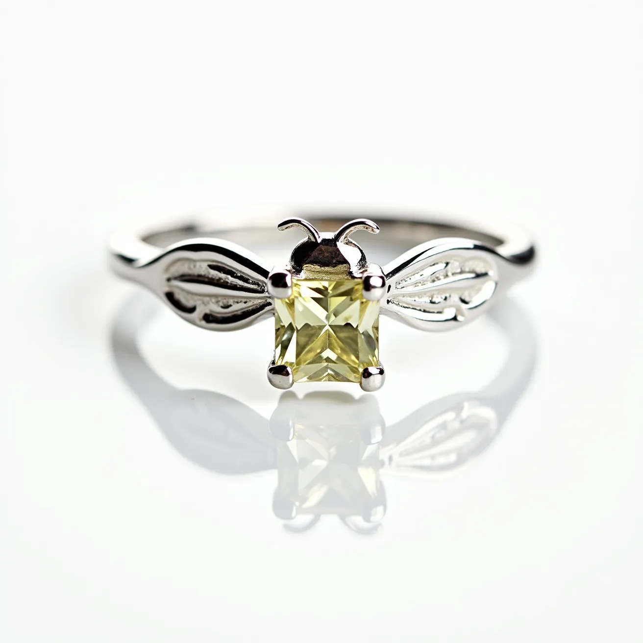 This bee ring showcases an elegant design featuring a central square-cut yellow gemstone that resembles a bee's body, securely set in a four-prong setting. The wings of the bee are crafted from a shiny metal, likely silver or white gold, which adds a modern and sleek touch to the piece. The attention to detail in the ring's construction highlights the delicate design, with smooth curves forming the bee's wings and antennae on either side of the gemstone. The band complements the intricate bee motif, contributing to the overall thematic harmony and artistic charm of the ring.