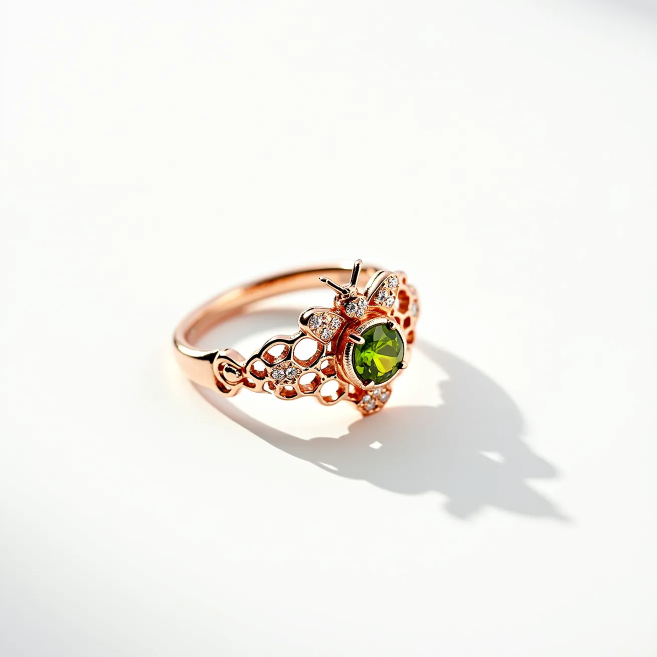 This bee ring showcases an intricate design crafted from what appears to be rose gold, highlighted by a vibrant round-cut green stone, possibly a peridot, set securely at the center surrounded by a bee motif. The wings and other details of the bee are adorned with small white stones, likely diamonds or cubic zirconia, set in a pavé style, adding sparkle and enhancing the bee's form. The openwork design on the band gives the ring a delicate, airy appearance, complementing the bee motif. The combination of the green stone and white stones with the rose gold material creates an elegant and nature-inspired piece of jewelry.