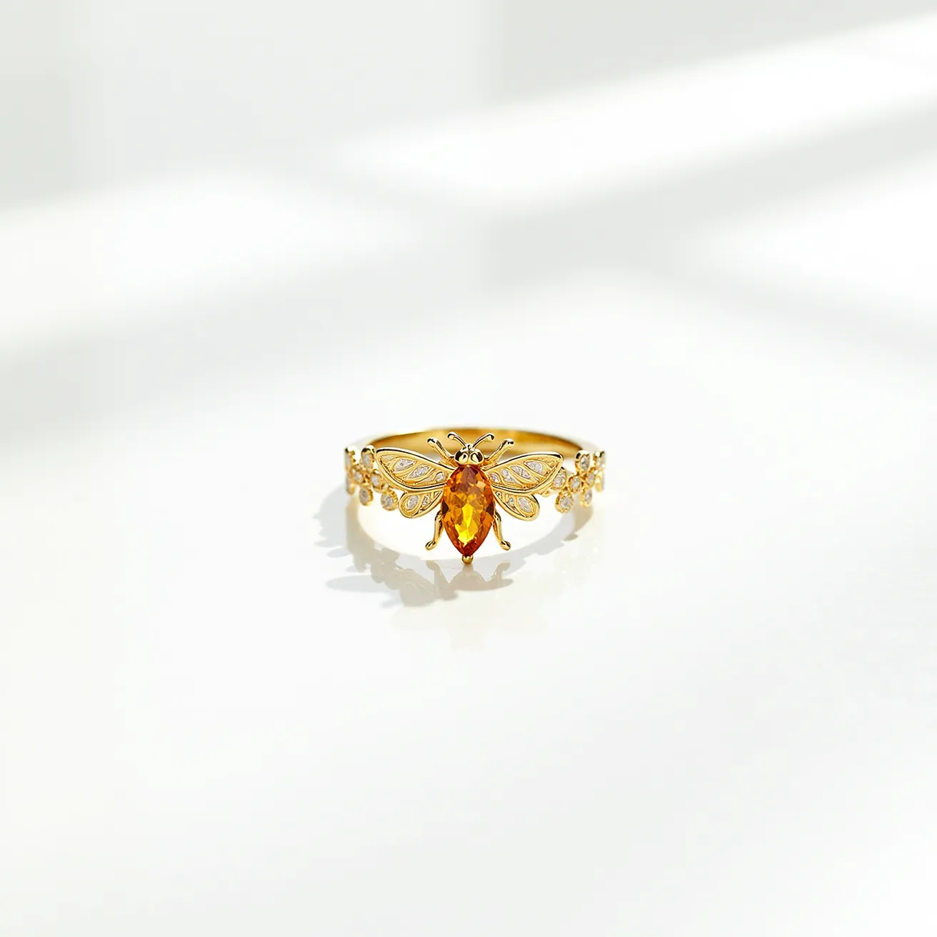 This bee ring features a detailed design crafted in a golden metal, likely gold or a gold-plated material. The central focus of the ring is a bee with an elongated, marquise-cut orange stone representing its body, suggesting it might be a citrine or another similarly hued gemstone. The wings are adorned with smaller stones, possibly diamonds or cubic zirconia, set in a pavé style to add intricate sparkle. The band continues this motif with additional small stones set along its sides, enhancing the elegance of the piece. The ring's structure does not visibly feature a clasp, as it is designed to be worn as a slip-on piece.