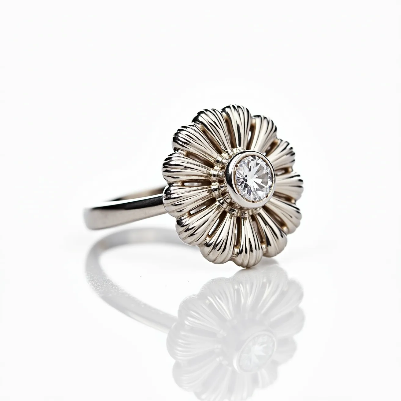 This big ring features a beautifully crafted flower design, made of metal, likely silver or white gold. At its center, a round brilliant-cut diamond is securely set in a bezel setting, which enhances the stone's sparkle while providing excellent protection. The petals are intricately detailed with ribbed texturing, giving the piece a dynamic and elegant appearance. The band is sleek and polished, complementing the ornate floral motif of the ring's top.