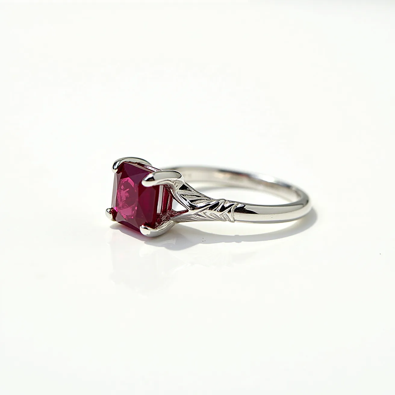 This big ring features a vibrant red gemstone, likely a ruby, cut in a square shape and secured in a four-prong setting. The setting is crafted from a silver-toned metal, potentially white gold or platinum, which adds a sleek and elegant touch to the piece. The band is adorned with delicate, engraved detailing, contributing to its refined appearance. Overall, the design emphasizes both the bold presence of the gemstone and the intricate craftsmanship of the metalwork.