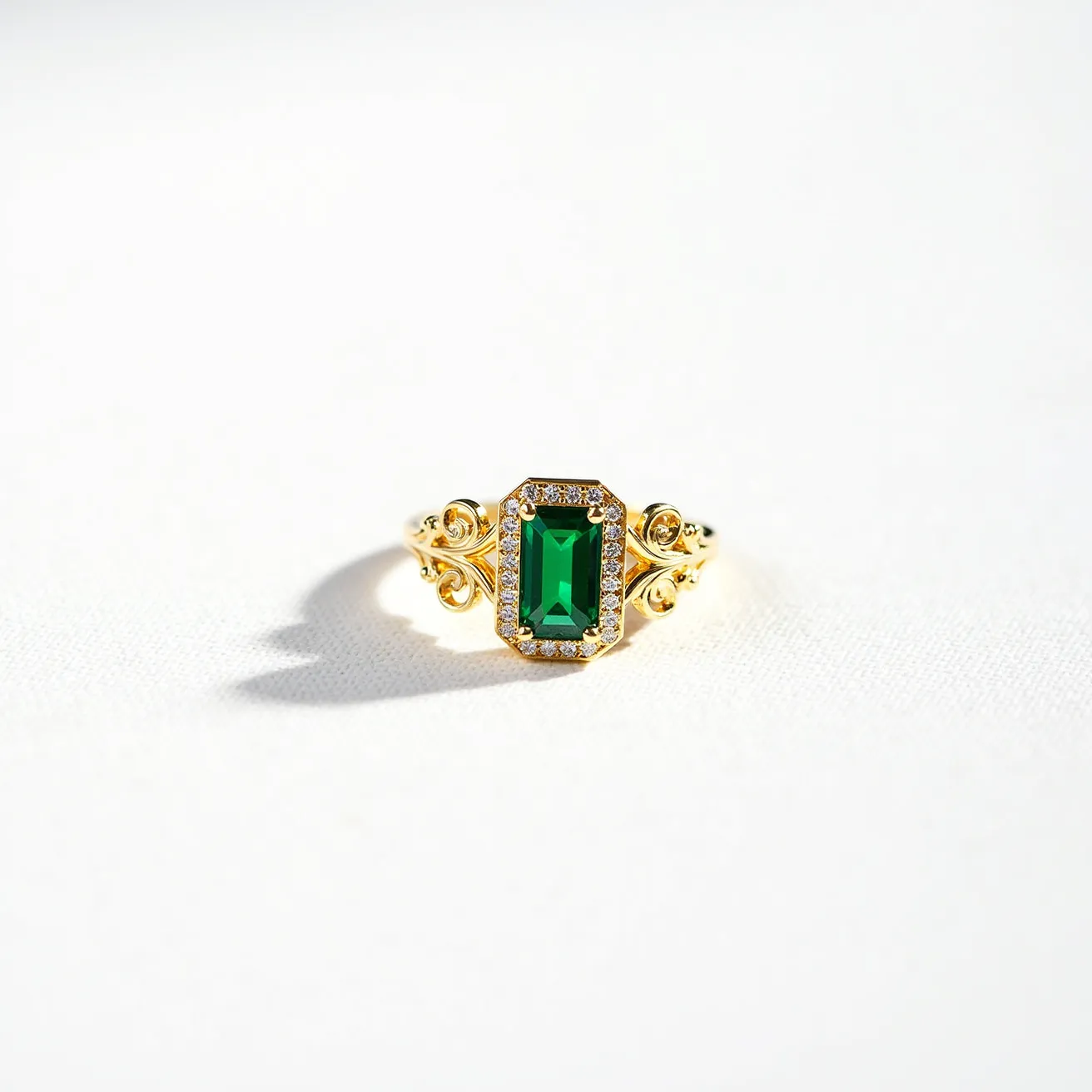 This big ring features a prominent rectangular emerald-cut green gemstone as its centerpiece, surrounded by a delicate halo of small, clear round stones, which appear to be diamonds. The setting of the ring is crafted from a lustrous gold material, showcasing intricate scrollwork designs on either side of the central stone. The design of the band complements the ornate appearance of the setting, and the ring showcases a seamless and elegant finish without any visible clasps or attachments.