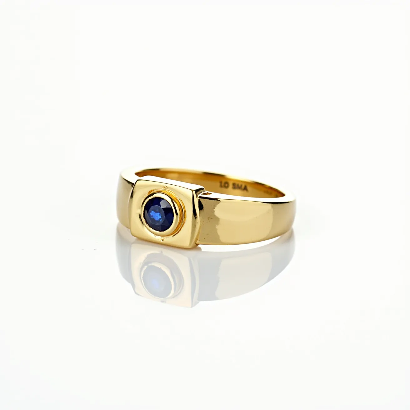 This big ring features a wide band crafted from a polished yellow metal, likely gold, which gives it a luxurious and classic appearance. The central focus of the ring is a round, deep blue gemstone, possibly a sapphire, that is set within a bezel setting, providing a secure and smooth finish. The stone's deep hue contrasts elegantly with the golden band, enhancing its visual appeal. The ring does not appear to have any clasps or additional attachments, maintaining a sleek and seamless design throughout.