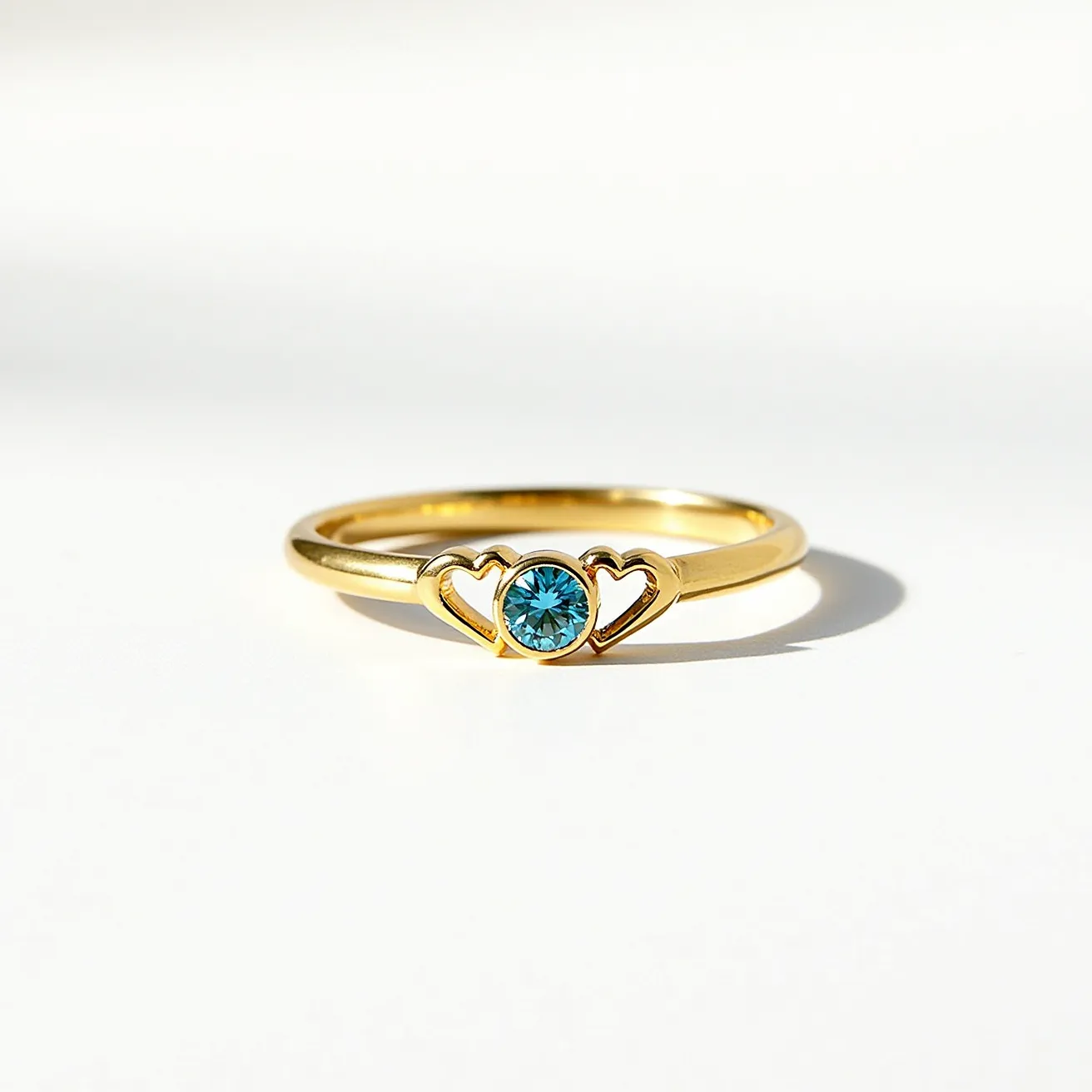 This birthstone ring features a slender band crafted from polished gold, showcasing a central round-cut blue gemstone. The stone is securely set within a bezel setting, elegantly framed by two symmetrical heart-shaped designs on either side. The gold finish and the gemstone's vibrant blue create an eye-catching contrast, highlighting the delicate artistry of the ring's design.