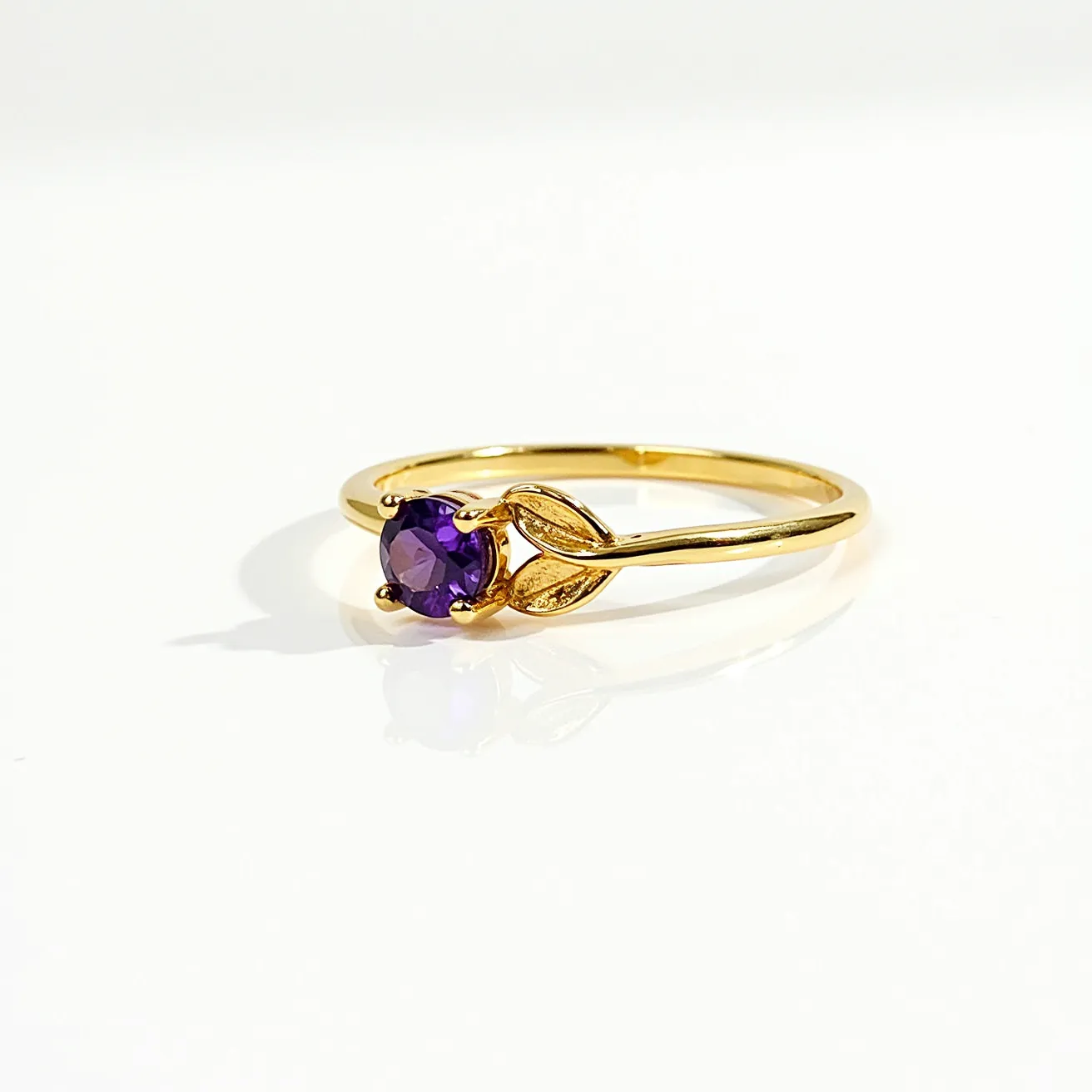 This birthstone ring features a gold band with a striking amethyst stone at its center. The amethyst, cut into a round shape, is set in a prong setting that securely holds the gemstone in place while allowing light to pass through, enhancing its purple hue. The design includes delicate leaf motifs flanking the stone, adding an elegant touch to the overall appearance. The simplicity of the band complements the vibrant stone, making this ring a tasteful and refined piece of jewelry.