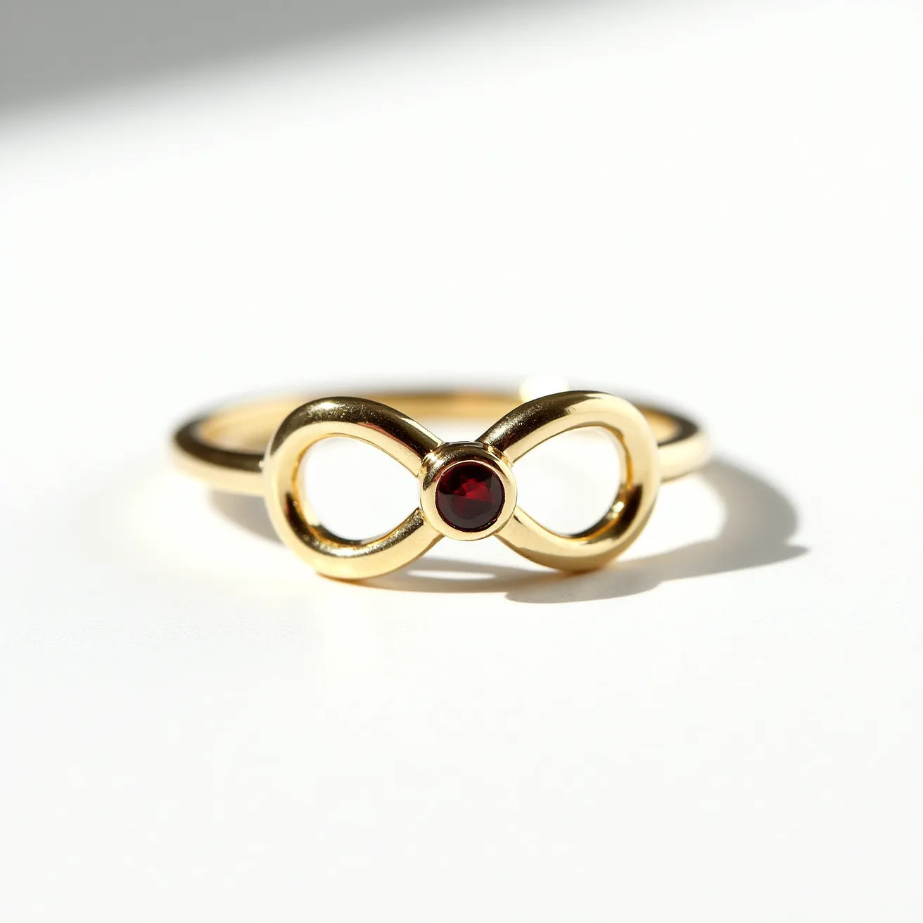 This birthstone ring features a sleek gold band with an elegant infinity design at its center. Nestled within the loop of the infinity symbol is a round, deep red garnet gemstone, expertly cut to enhance its luster and set securely in a bezel setting. The garnet, representing the birthstone for January, adds a rich, vibrant color to the sophisticated design of the ring. The simplicity of the single gemstone combined with the infinity motif creates a timeless elegance, making it suitable for both everyday wear and special occasions.