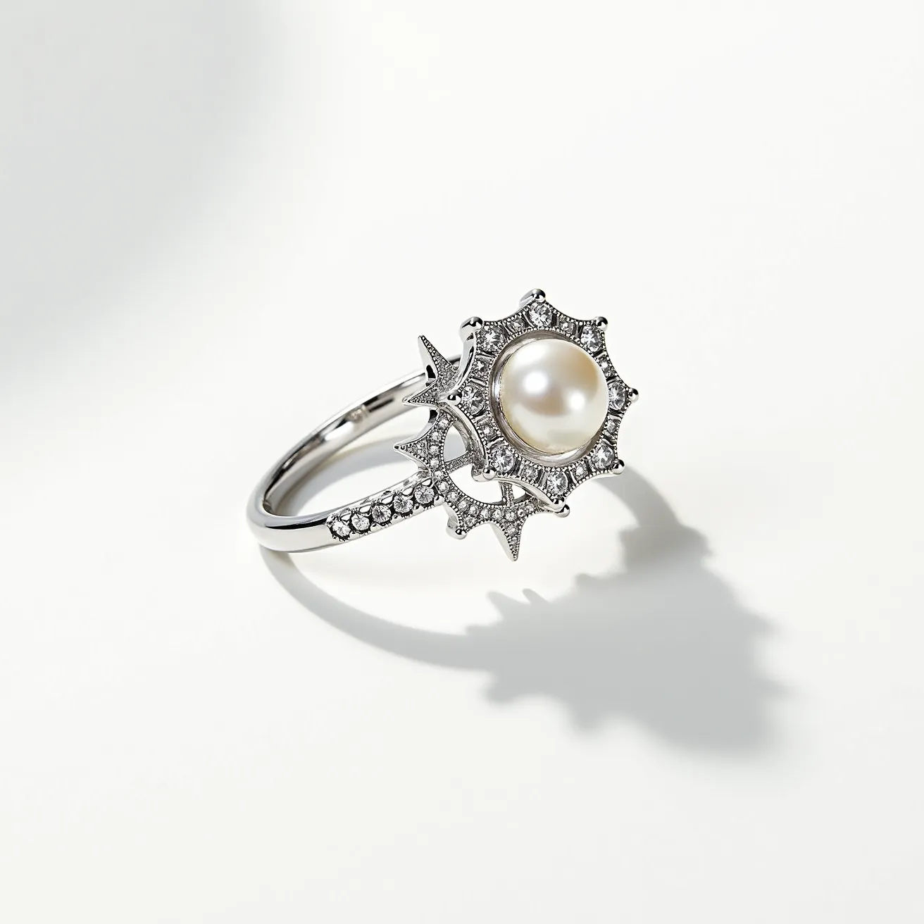 This birthstone ring showcases an elegant design featuring a central pearl, renowned for its lustrous and classic appeal. The pearl is round and prominently set in the center, surrounded by a decorative halo of small, sparkling stones set into an intricate metalwork that enhances its celestial theme. The band itself appears to be made of a polished silver or white gold, complementing the luminous quality of the pearl and the surrounding gems. The intricate details and craftsmanship suggest a sophisticated and timeless piece.