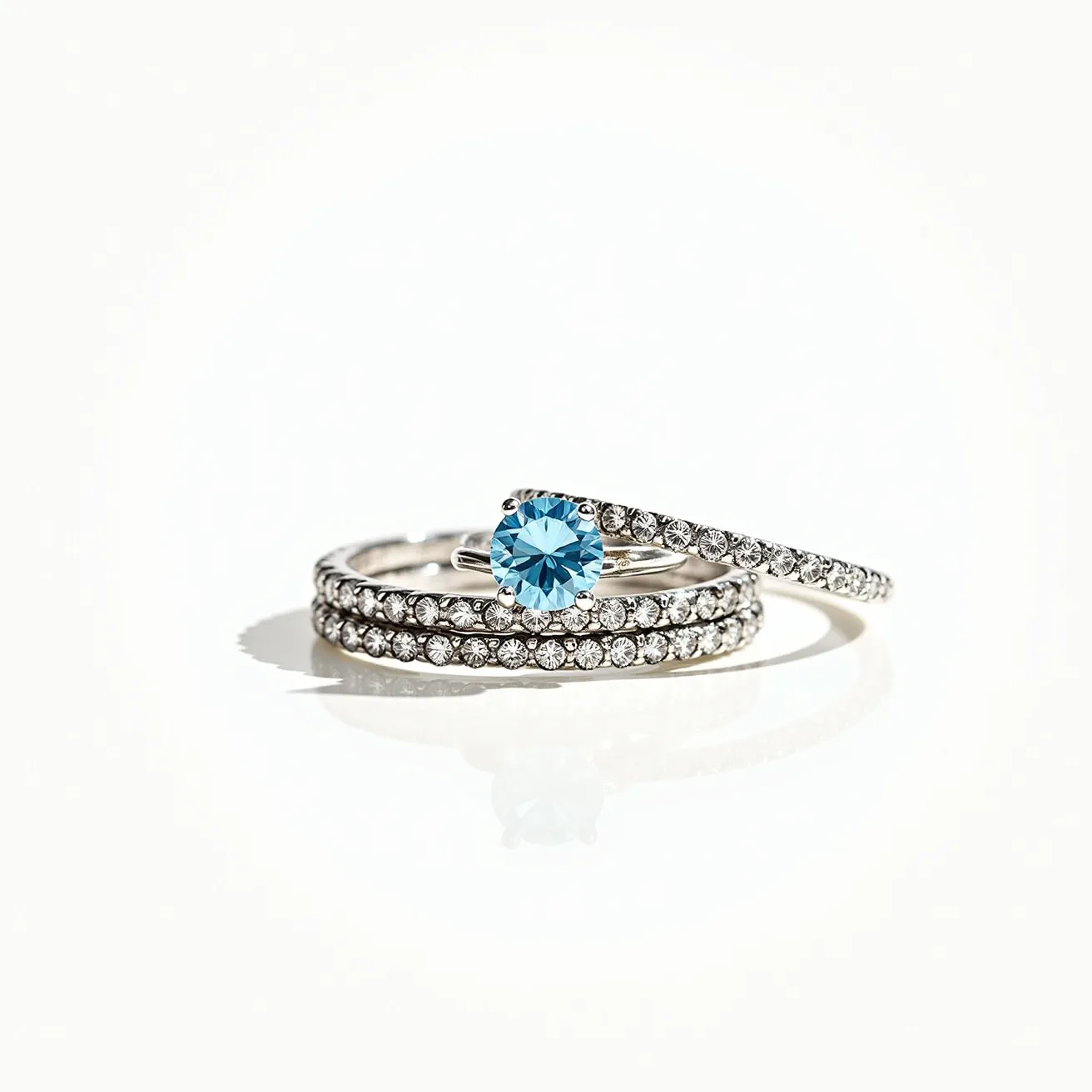 These birthstone stackable rings feature elegant materials, including a lustrous metal band, likely white gold or platinum, which provides a polished and sophisticated base. The central highlight of the set is a striking blue gemstone, possibly a blue topaz or aquamarine, cut in a brilliant round shape and set prominently in a raised prong setting that allows light to pass through, enhancing its sparkle. Surrounding this center stone, smaller, clear stones are meticulously set in a pavé style along the bands, adding a continuous shimmer. Each ring fits seamlessly together, enhancing the overall aesthetic when worn in combination, embodying simplicity and elegance without requiring any clasps or attachments.