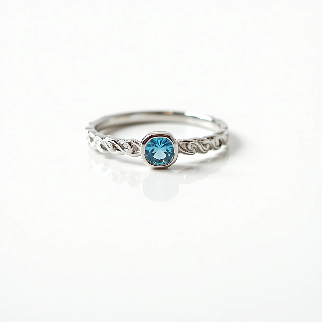 This birthstone stackable ring features a sleek metal band with a delicate twisted design, likely crafted from sterling silver or white gold. The ring showcases a round-cut blue gemstone, possibly a blue topaz, set in a bezel setting which securely encases the stone. The minimalist design emphasizes the gemstone's vibrant color, allowing it to stand out as the ring’s focal point. The band is smooth and designed to allow for easy stacking with other rings.