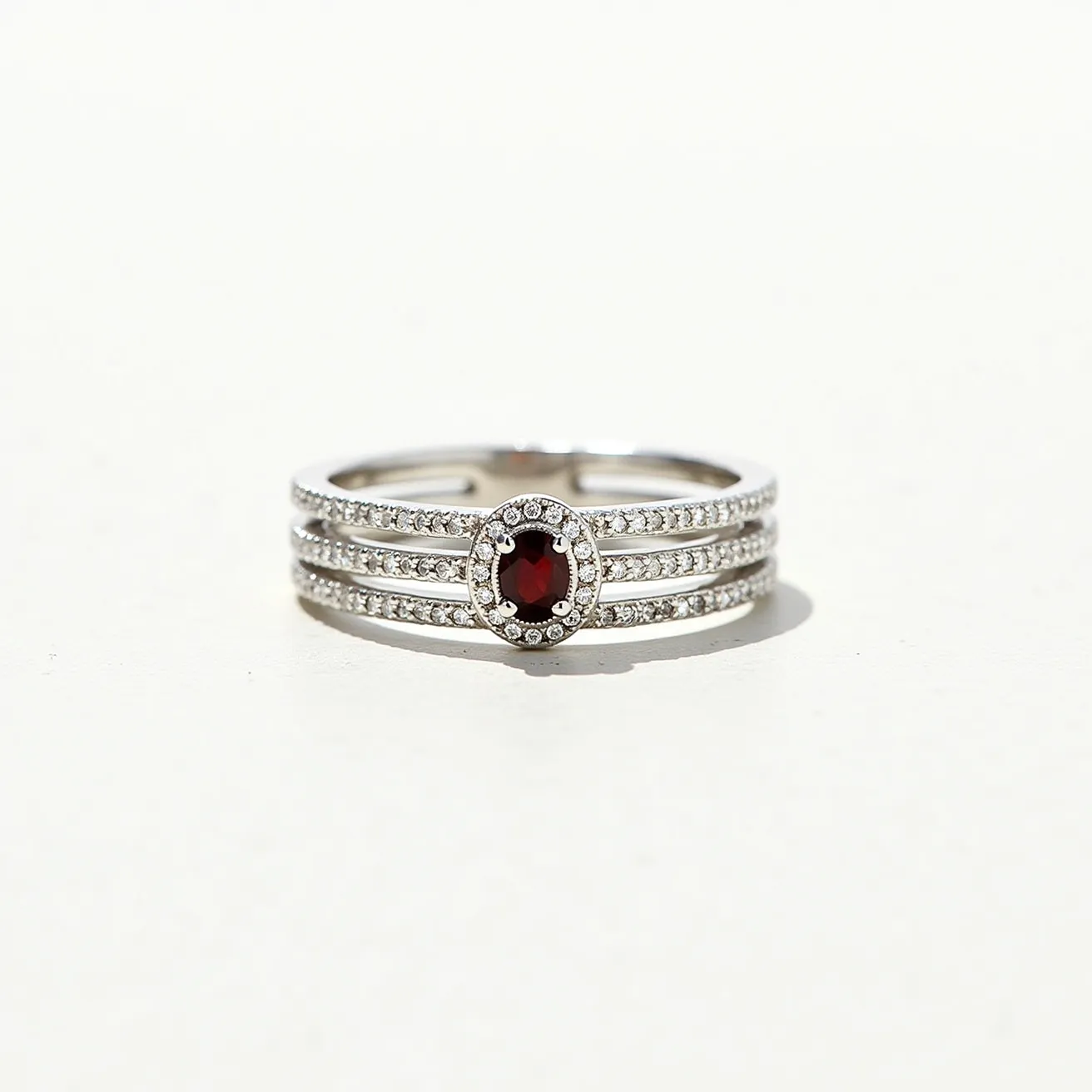 These birthstone stackable rings feature three elegant bands meticulously crafted from what appears to be a polished silver metal, creating an exquisite and versatile piece of jewelry. Each band is delicately adorned with small, round-cut white stones, possibly diamonds or cubic zirconia, set in a classic prong setting that enhances their sparkle. At the center of the ensemble is an oval-cut, deep red gemstone, likely a garnet representing the January birthstone, securely set in a halo of matching white stones. The overall design allows for seamless stacking, making it both a stylish and meaningful accessory.