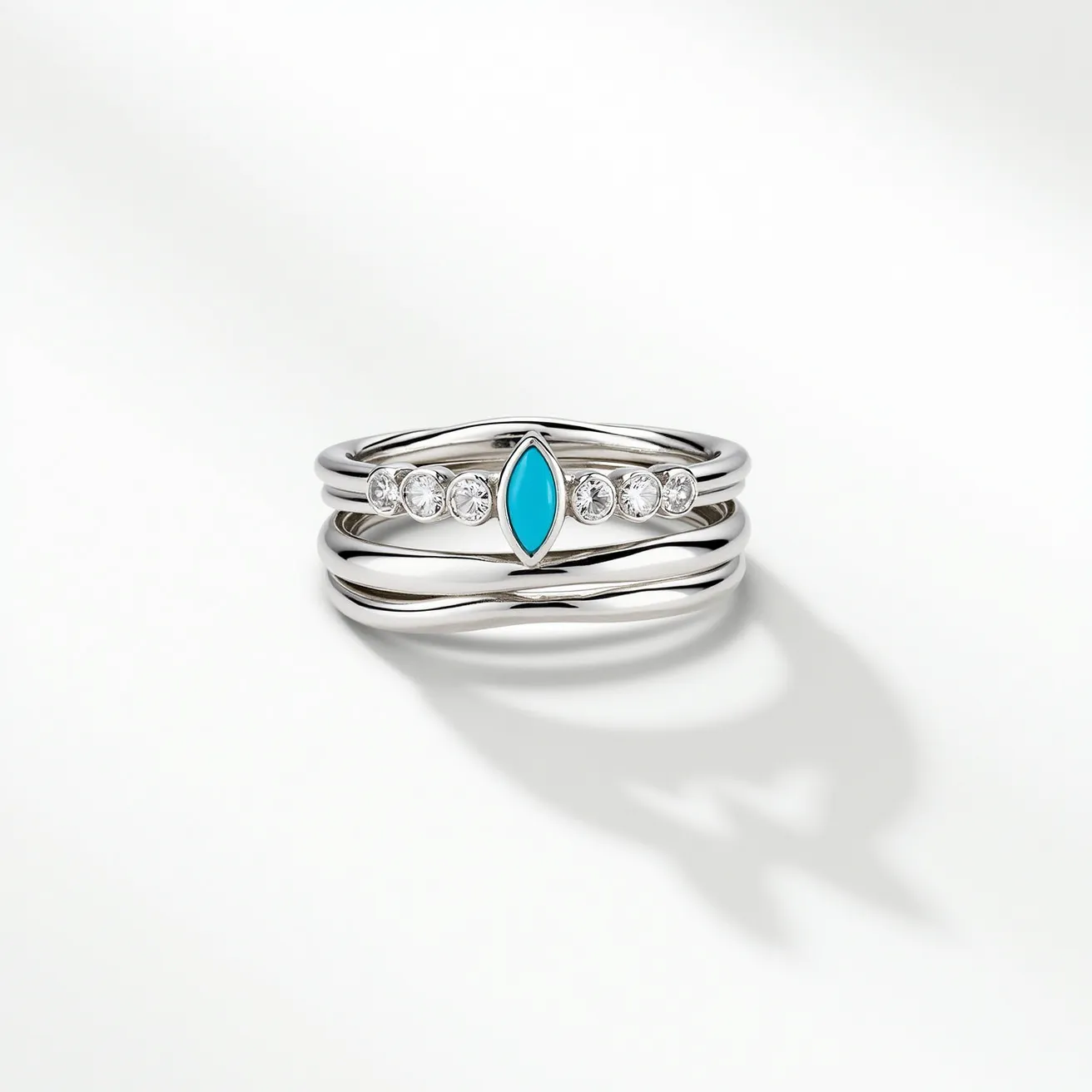 These birthstone stackable rings are crafted from a polished silver material, displaying a sleek and modern aesthetic. The central ring features a distinctive marquise-cut turquoise stone set horizontally, accompanied by five small round brilliant-cut clear gemstones on each side, suggesting diamond or diamond-like accents. The stones are securely bezel-set, adding an elegant touch to the design. The remaining rings are simple, smooth bands, perfectly complementing the adorned ring, allowing each piece to be worn individually or stacked for a layered effect. These rings showcase a refined blend of color and sparkle, ideal for personal expression or gifting.