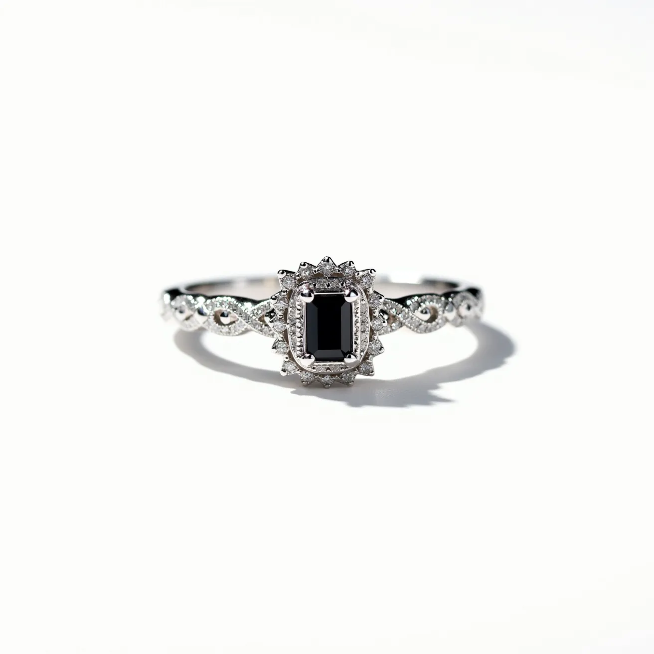 This black diamond ring features a central emerald-cut black diamond set in a stunning halo of smaller white diamonds. The band, likely crafted from white gold or platinum, showcases intricate filigree detailing that enhances its elegance and sophistication. The setting holds the central stone securely, while the additional diamonds add to its overall sparkle and allure. The craftsmanship highlights both the contrast and harmony between the dark hue of the black diamond and the vibrant brilliance of the surrounding stones.