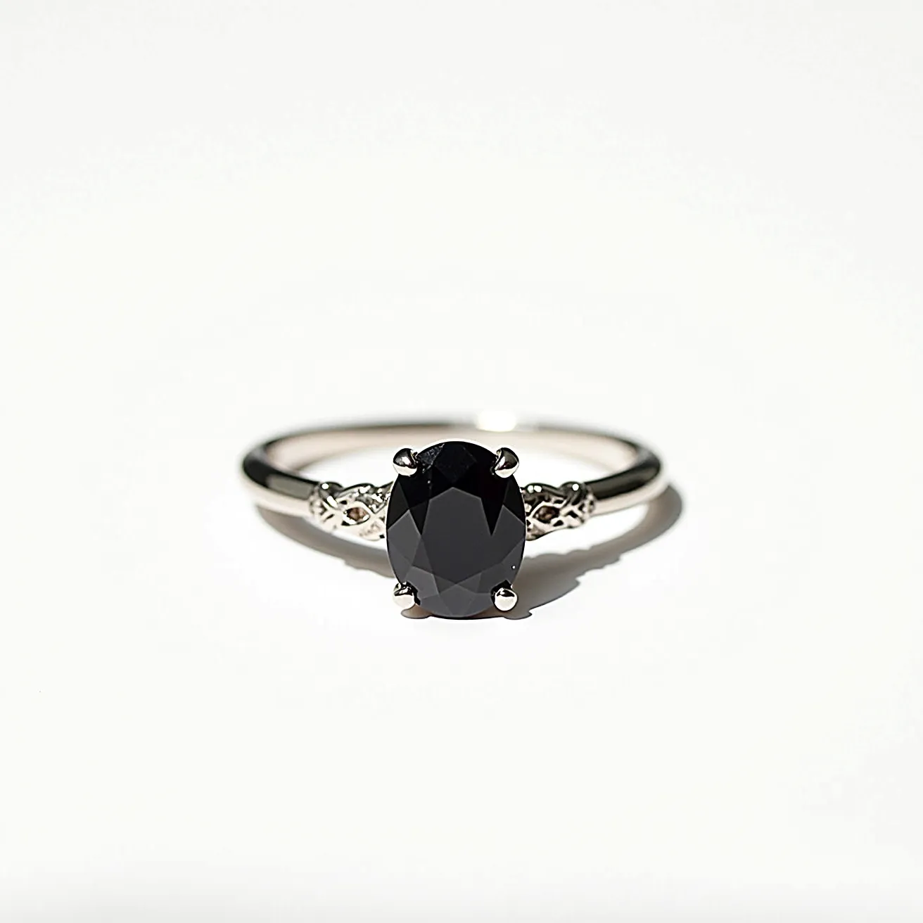 This black diamond ring features a striking oval-cut black diamond as its centerpiece, set in a classic four-prong setting. The band is crafted from a polished metal, possibly white gold or platinum, which complements the deep hue of the diamond, adding a touch of elegance to the overall design. The shank incorporates intricate detailing adjacent to the setting, providing a subtle yet sophisticated accent to the ring. The combination of the black diamond and the refined metalwork creates a timeless piece that exudes both modernity and elegance.