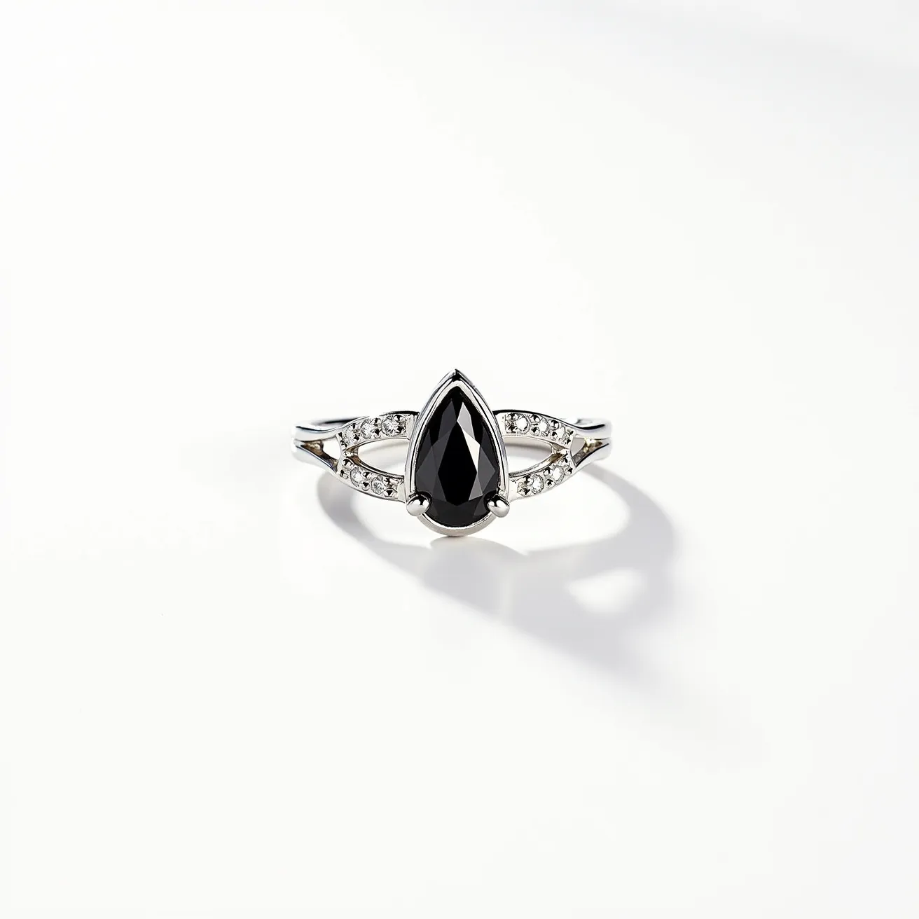 This black diamond ring features a striking pear-shaped black diamond as the centerpiece, set in a polished metal band that may be platinum or white gold. The central stone is accentuated by smaller round white diamonds embedded in the band on each side of the main gem, enhancing its elegance and providing a contrasting sparkle. The setting appears to be a prong design, securely holding the central diamond while allowing maximum light exposure to highlight the gem's facets. The band is sleek with a smooth finish, providing a sophisticated and modern appeal to the overall design.