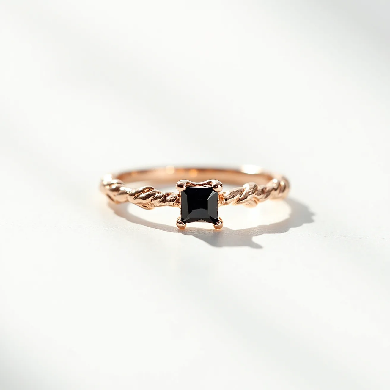 This black diamond ring features a striking square-cut black diamond set as the central stone, held securely by a classic four-prong setting. The band is crafted from rose gold, showcasing an intricate twisted design that adds a touch of elegance and uniqueness to the piece. The choice of materials and design creates a harmonious balance, highlighting the black diamond's bold and sophisticated allure.