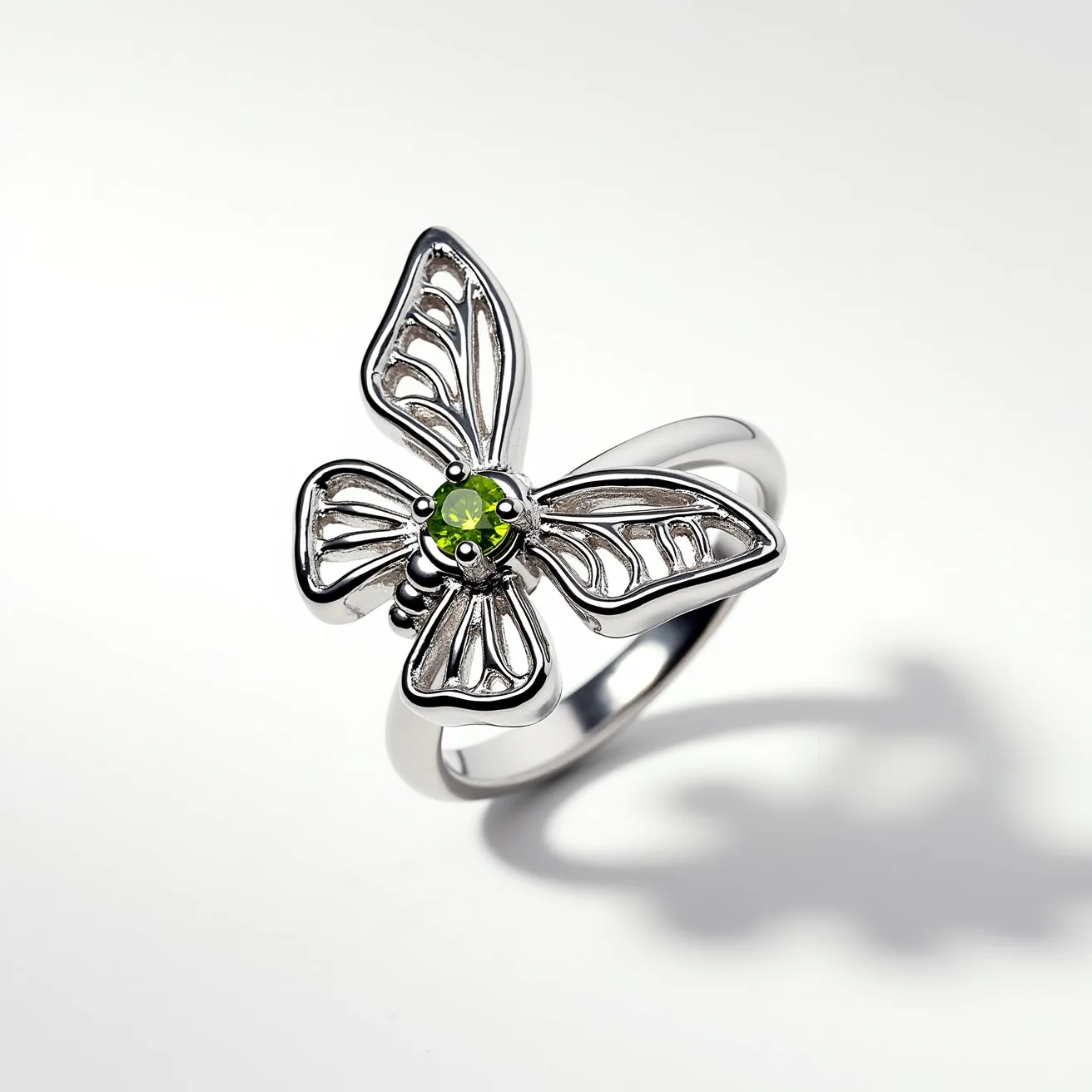 This butterfly ring features a polished silver setting, capturing the delicate form of a butterfly with detailed, openwork wings. At the center, a vibrant green gemstone is set, possibly a peridot, crafted in a round cut that catches the light beautifully. The gemstone is secured with a classic prong setting, enhancing its visibility and sparkle. The band is smooth, contributing to the overall elegance and fluidity of the design, with no additional clasps or attachments present.