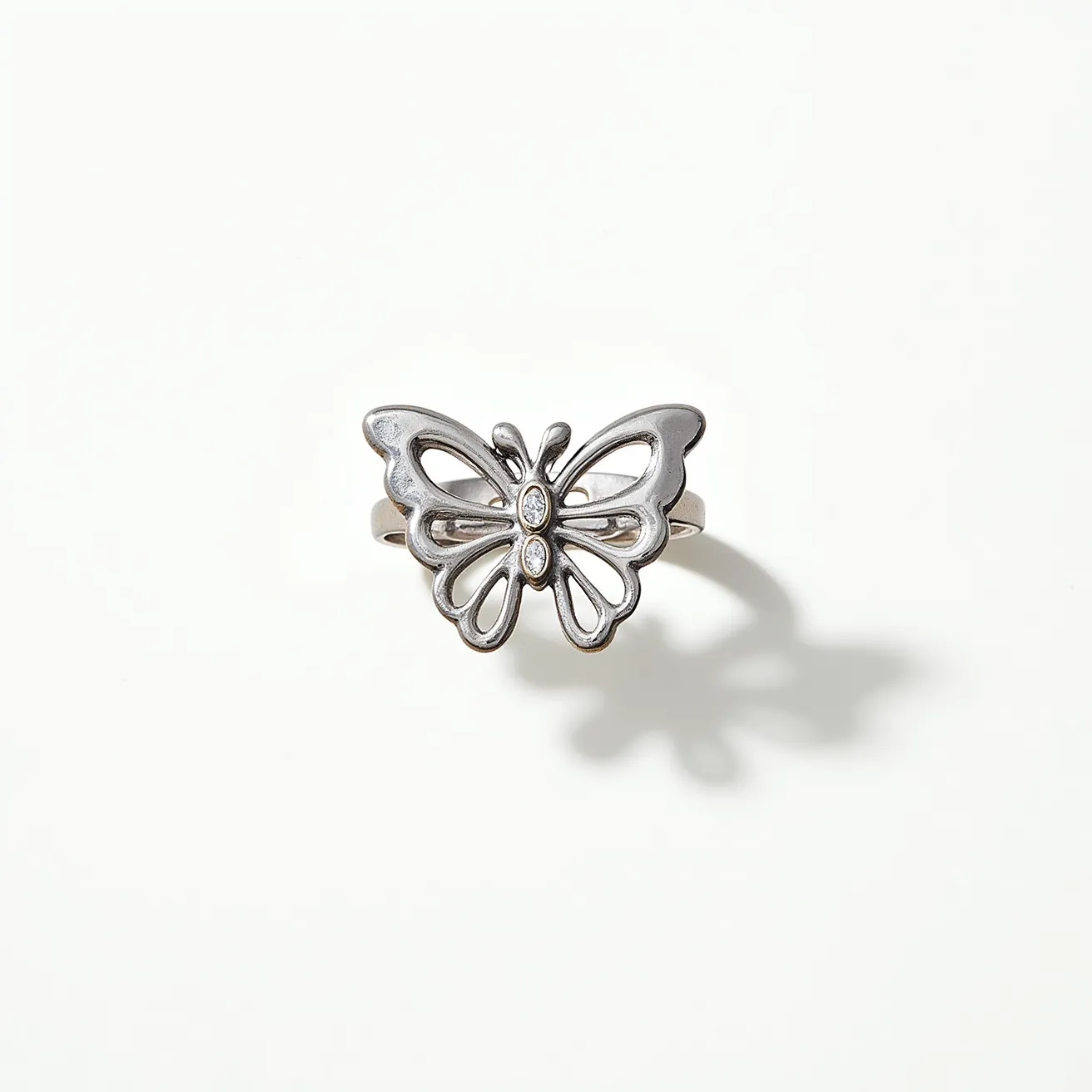 This butterfly ring features a delicate design crafted from a silver or platinum-like metal, with graceful and open lacy wings that give it an elegant appearance. The ring is adorned with three clear, oval-cut gemstones set vertically in the center of the butterfly, likely diamonds, which add a sparkling focal point to the piece. The stones are securely held in a bezel setting, enhancing the ring's sleek and modern aesthetic. The band appears to be a simple, polished band that complements the intricate butterfly design without any additional clasps or attachments, preserving the ring’s symmetry and sophistication.