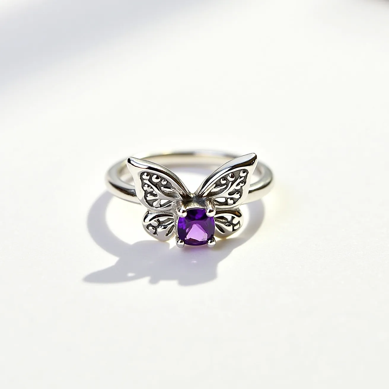 This butterfly ring features a delicate design crafted primarily from a silver-toned metal, forming the intricate wings of the butterfly. At the center of the butterfly's body is a prominent square-cut purple gemstone, possibly an amethyst, securely held in place by prong settings. The silver filigree detailing adds elegance to the wings, enhancing the visual appeal of the piece. The band of the ring is smooth and round, complementing the ornate design of the butterfly while providing a comfortable fit.