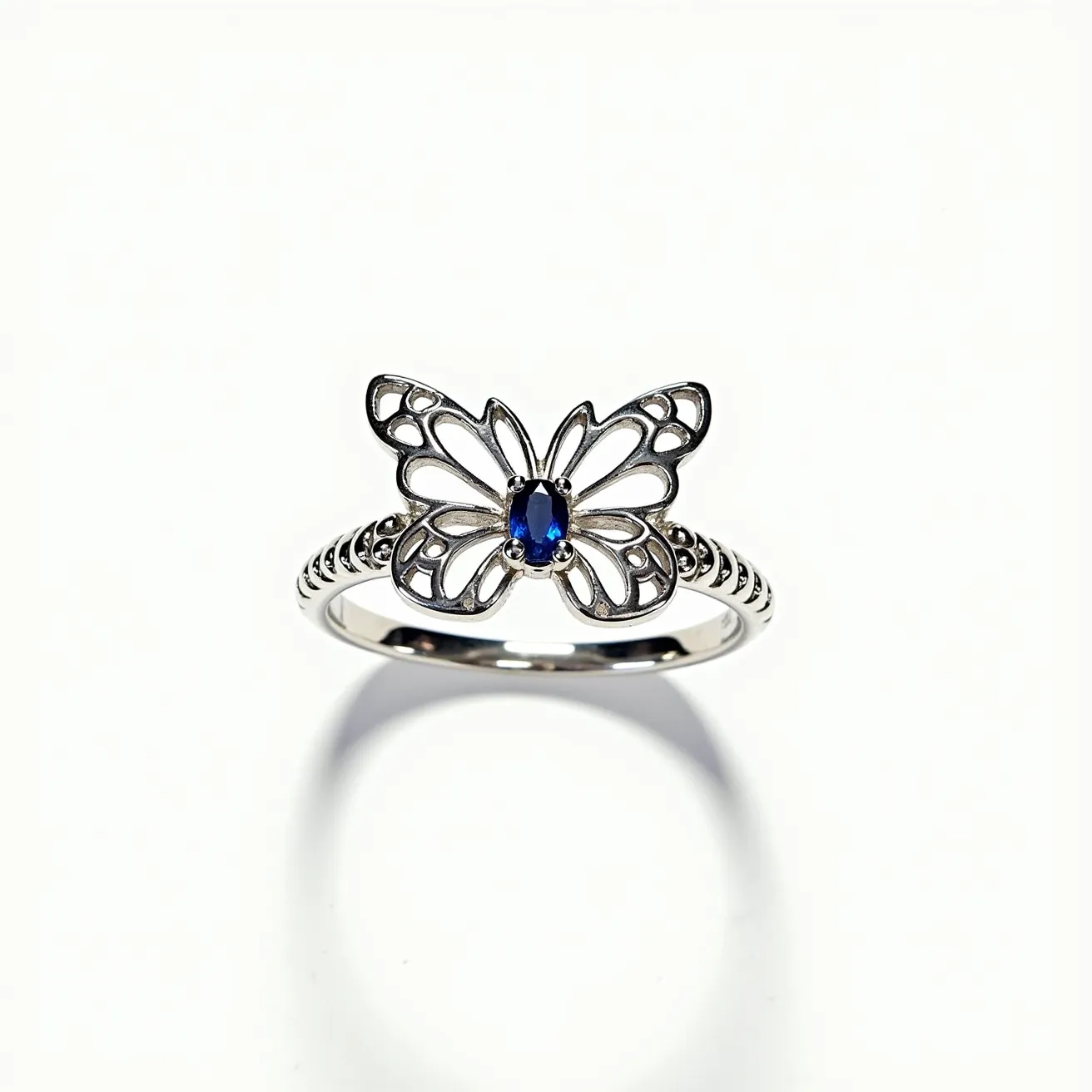 This butterfly ring features an elegant design crafted from what appears to be sterling silver, forming the shape of a butterfly with delicate, openwork wings. At the center of the butterfly, there is a small, oval-cut blue gemstone, likely a sapphire, set in a bezel style which securely holds the stone while allowing light to enhance its color and luster. The band is adorned with subtle beaded detailing that adds texture and interest to the overall design. The ring combines both artistry and craftsmanship, creating a piece that is both whimsical and sophisticated.