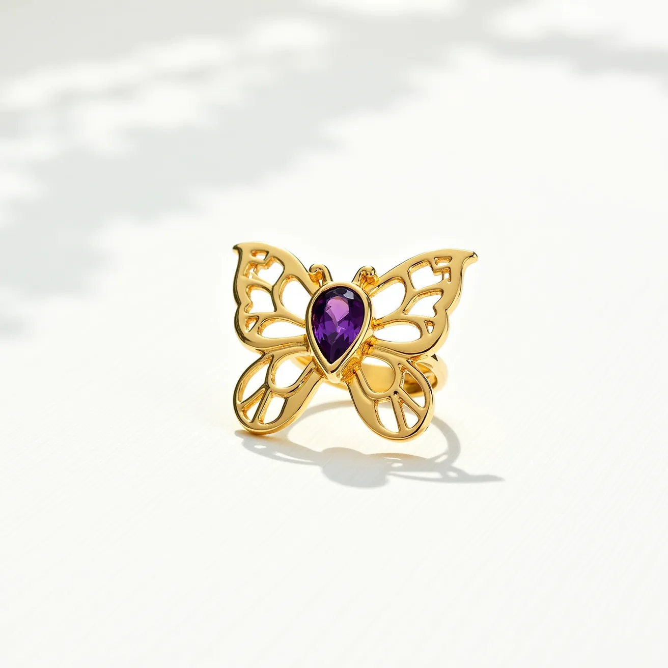 This butterfly ring features an elegant design, crafted from a polished gold-toned metal that forms the intricate outline of a butterfly's wings. At the center, it is adorned with a teardrop-shaped amethyst stone, held securely in a bezel setting, adding a vibrant purple hue to the piece. The band of the ring is seamlessly integrated with the butterfly motif, creating a harmonious and sophisticated look without any visible clasps or attachments. The combination of the gold metal and the deep-colored gemstone provides a striking contrast, enhancing the overall visual appeal.