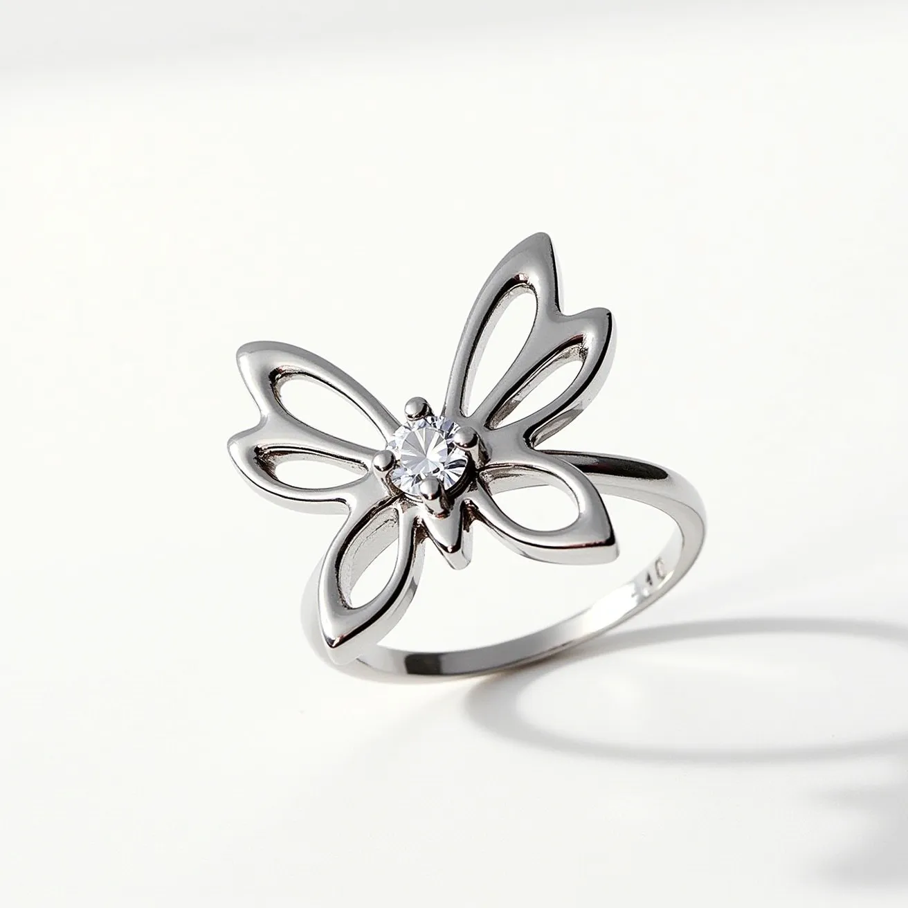 This butterfly ring showcases a sleek, metallic band, likely made of silver or white gold, which gracefully forms an open butterfly design. At the center of the butterfly is a round-cut gem, likely a diamond or a diamond simulant, which is prong set for security and prominence. The openwork design of the wings provides a delicate and airy appearance. The band appears smooth, ensuring comfort and ease of wear. This ring does not include any additional clasps or attachments, as it is designed to be worn as a standard ring, highlighting the elegance and simplicity of its design.