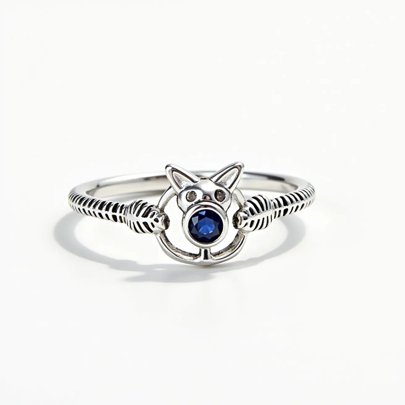 This cat ring is crafted from a silver-toned metal, featuring a central design that mimics a cat's face with pointed ears. The ring is adorned with a single round, faceted blue gem, prominently placed in the center, likely using a bezel or prong setting. The band shows a coiled or ribbed texture, enhancing the ring's visual appeal, and appears to seamlessly integrate with the cat motif without any visible clasp or distinct attachment.