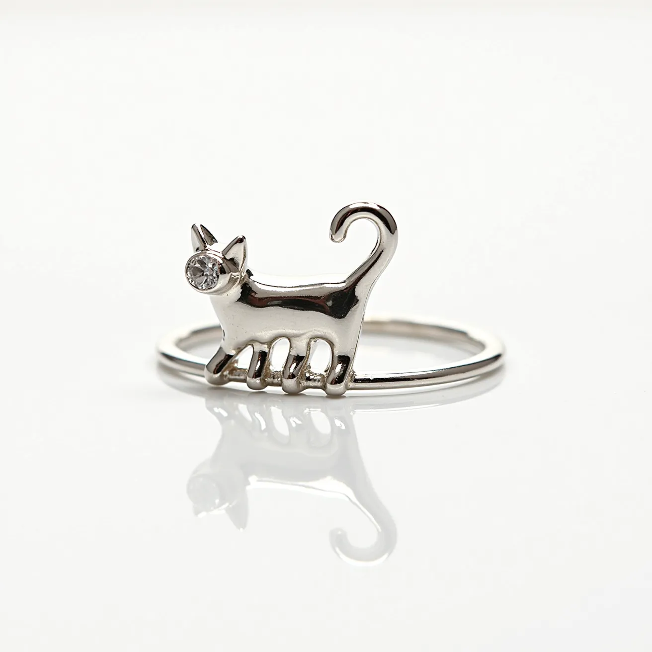 This cat ring features a minimalist design with a sleek, polished metal finish, likely crafted from silver or white gold. The cat figure is artfully created with a graceful arch in its tail and streamlined body form. A single, small round-cut gem, possibly a diamond or cubic zirconia, is set into the cat's eye, providing a subtle sparkle and enhancing the whimsical aesthetic of the piece. The stone is securely held within a bezel or prong setting, adding to the durability of the ring’s design. The band of the ring is delicate and continuous, with no additional clasps or attachments, maintaining a simple yet elegant appearance.