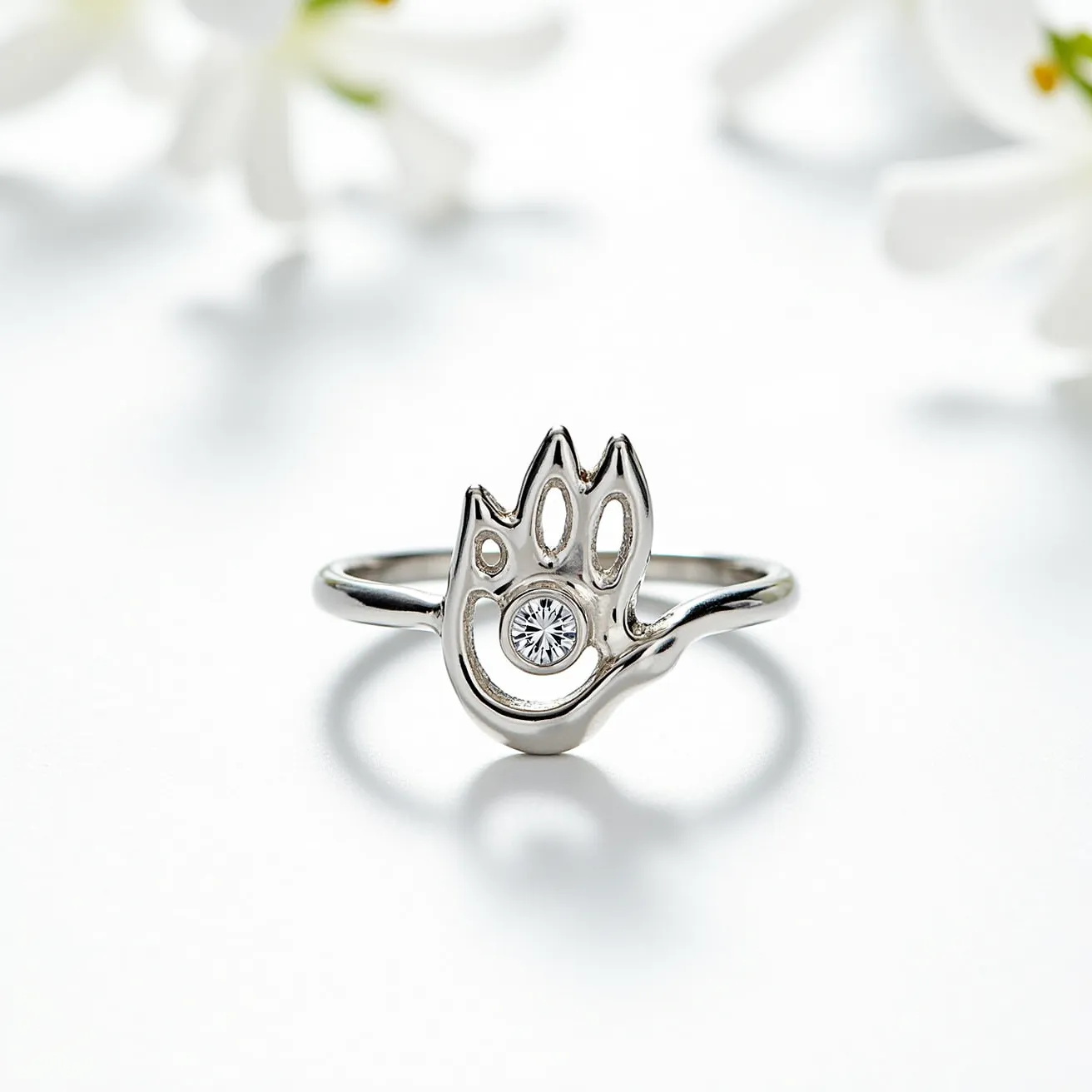 This cat ring features a minimalist design crafted from a reflective metal, possibly silver or white gold, showcasing a stylized cat paw motif as its central element. At the center of the paw design is a round, clear gemstone, likely a diamond or cubic zirconia, which is securely set into the metal. The stone is mounted in a bezel setting, providing a smooth finish and ensuring the gem is the focal point without prongs. The ring band is slender, complementing the subtlety of the central design, and lacks any additional clasps or attachments, indicating a simple slip-on style.