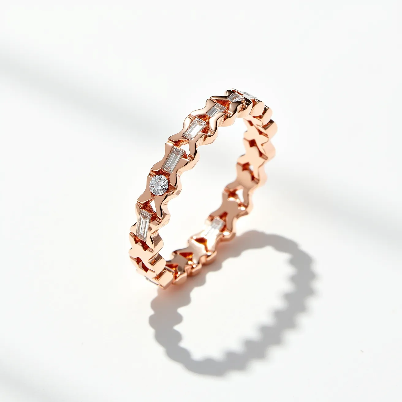 This chevron ring is crafted from rose gold, featuring a distinctive zigzag pattern that gives it its chevron shape. The ring is adorned with both baguette-cut and round-cut diamonds, each set elegantly within the gold framework. The diamonds are arranged alternately along the band, with the baguette-cut diamonds providing a sleek, elongated sparkle, while the round-cut diamonds offer a classic brilliance. The settings for the stones appear to be prong-style, securing the gems while maintaining a seamless and sophisticated look. The ring has a continuous band with no visible clasps or attachments, highlighting its elegant and uninterrupted design.