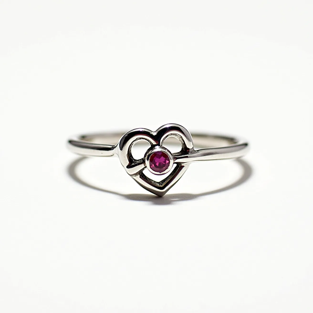 This Chrome Hearts ring features a silver band crafted into a heart design that elegantly showcases a single round-cut gemstone. The gemstone is a striking pink, likely a ruby or pink sapphire, set securely at the heart's center. The minimalist band complements the vibrant stone, enhancing its visual appeal without the need for additional clasps or attachments. The overall design exudes a blend of simplicity and sophistication, characteristic of Chrome Hearts' signature style.