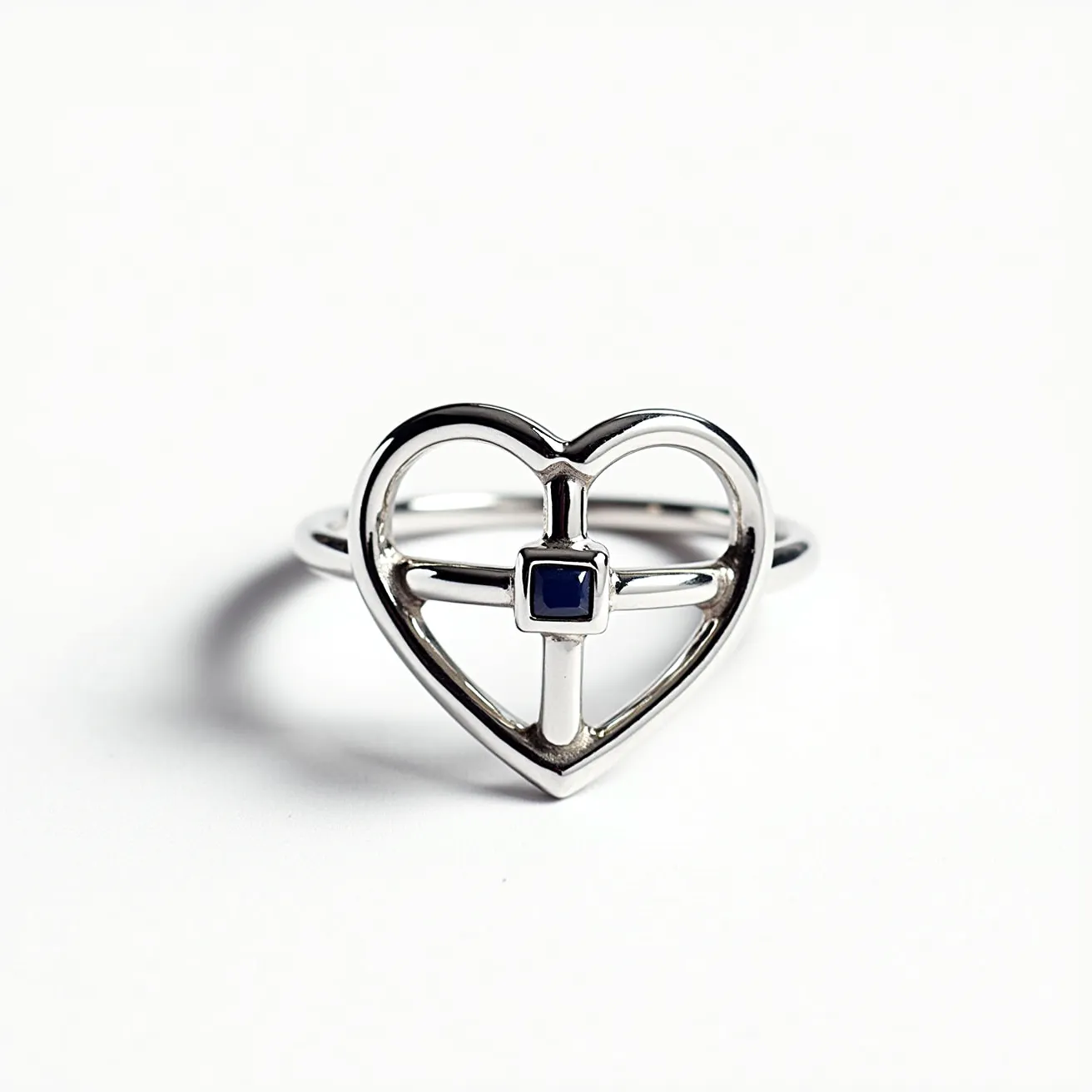 This Chrome Hearts ring features a heart-shaped design crafted from a polished metal, likely sterling silver, and incorporates a central cross motif. At the intersection of the cross, a small, square-cut blue gemstone is set in a bezel setting, adding a touch of color and elegance to the piece. The overall design is sleek and minimalistic, showcasing the craftsmanship characteristic of Chrome Hearts jewelry. The band smoothly integrates into the heart shape, ensuring comfort and wearability without the use of any clasps or attachments.