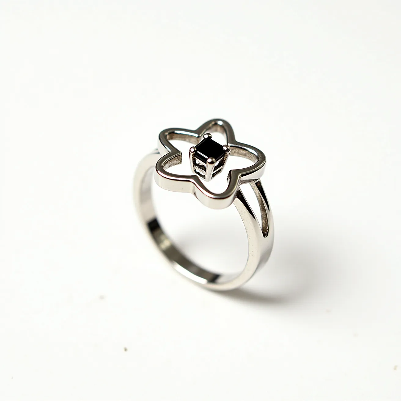 This Chrome Hearts ring features a polished metallic band with a unique flower-shaped design on top. At the center of the flower is a black gemstone, cut in a square shape, secured by a prong setting. The ring has a minimalist yet distinctive style, with the flower design creating an open, airy feel that highlights the central gemstone. The combination of the sleek metal and the dark stone provides a striking contrast, enhancing the visual appeal of the piece.