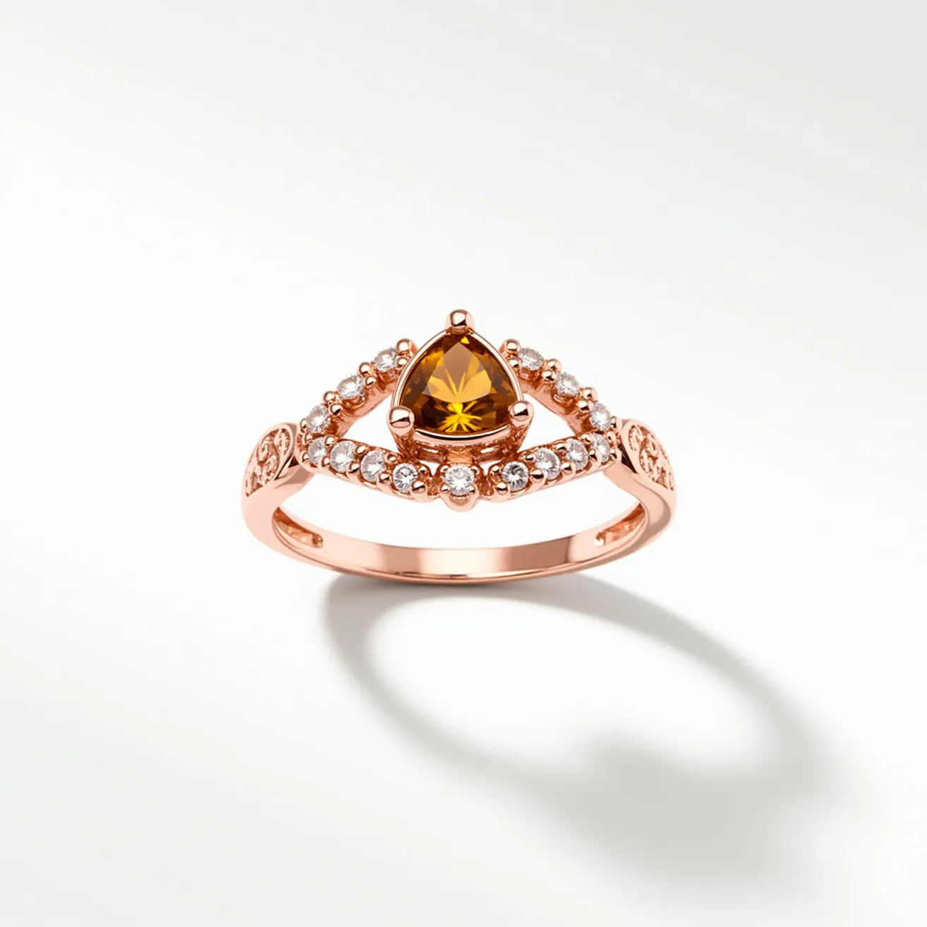 This citrine ring features a stunning trillion-cut citrine stone set in a prong setting at the center, bordered by a row of small round white gemstones, which are likely diamonds or cubic zirconia, that enhance its brilliance. The band is crafted from a rose gold metal, providing a warm and elegant contrast to the vibrant yellow-orange hue of the citrine. The design includes intricate detailing on the band, with decorative motifs that add to its sophistication.