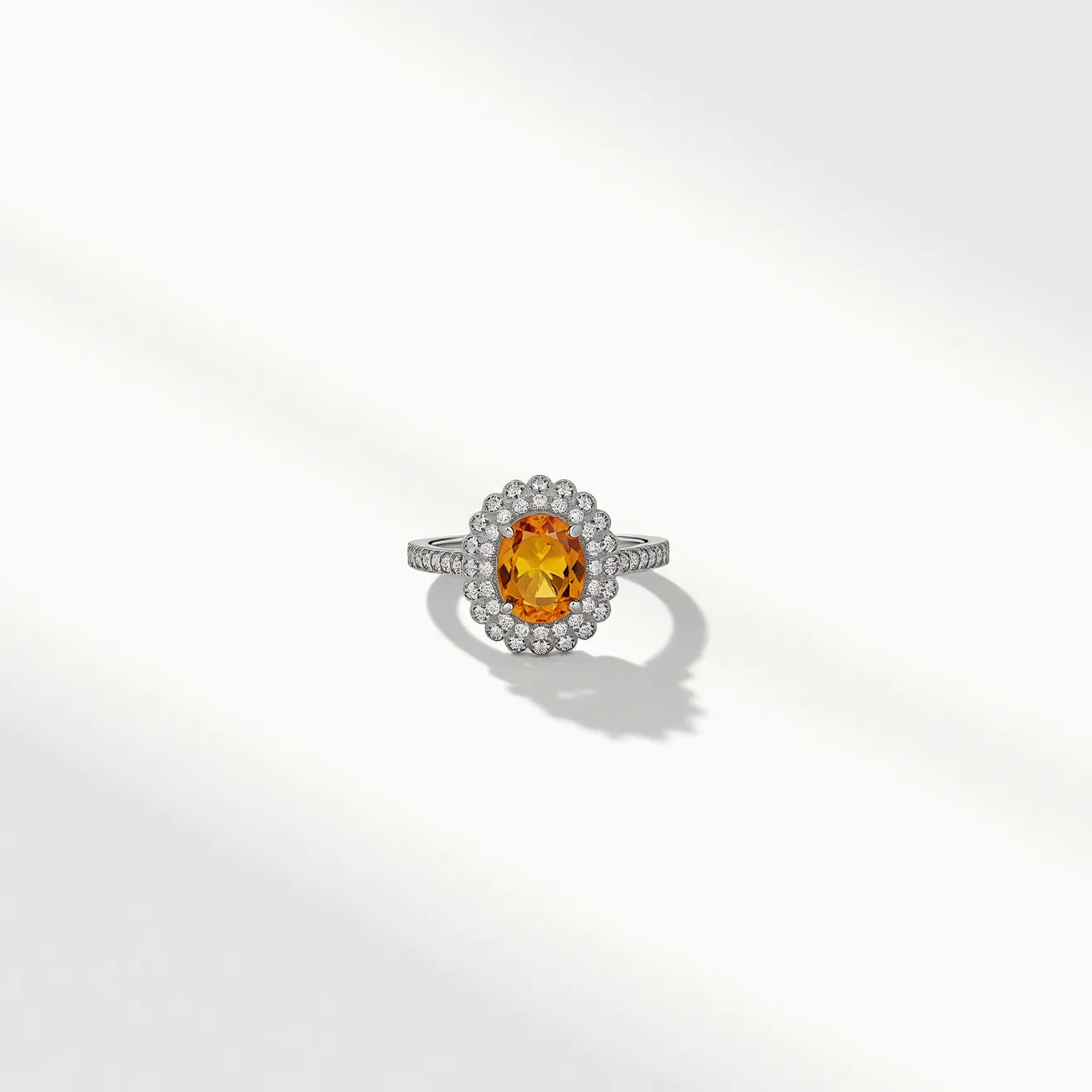 This citrine ring features a stunning oval-cut citrine as its centerpiece, showcased in a secure prong setting. The vibrant orange gemstone is surrounded by a halo of smaller, round-cut diamonds that enhance its brilliance. The band appears to be made of a polished metal, likely white gold or platinum, and is adorned with additional diamonds that are pave-set along the shoulders. The combination of materials and craftsmanship results in an elegant and sophisticated piece of jewelry.