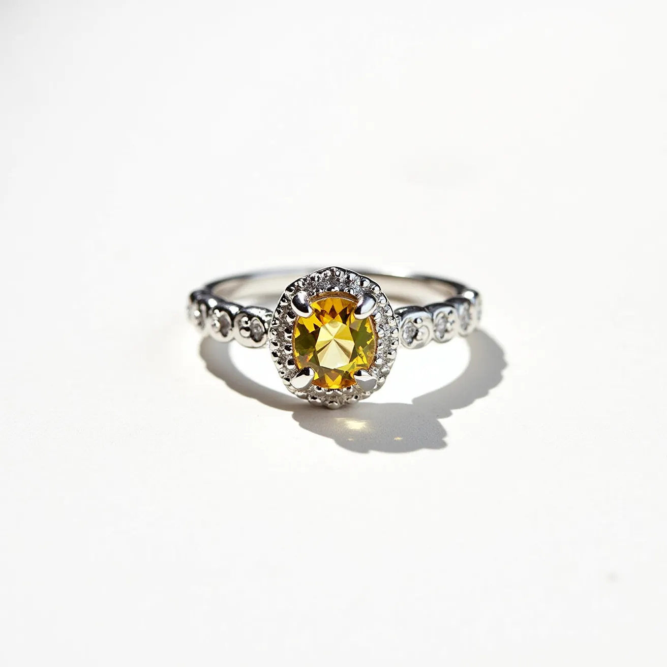 This citrine ring features a vibrant, round-cut citrine gemstone as its centerpiece, showcasing a brilliant yellow hue. The stone is elegantly set in a halo of pavé or bead-set clear stones, contributing to its sparkling appearance. The band is crafted from a polished metal, likely silver or white gold, and is adorned with additional small stones along the sides, enhancing the overall elegance and detail of the design. The setting appears secure, with prongs holding the central citrine in place, ensuring both beauty and durability.