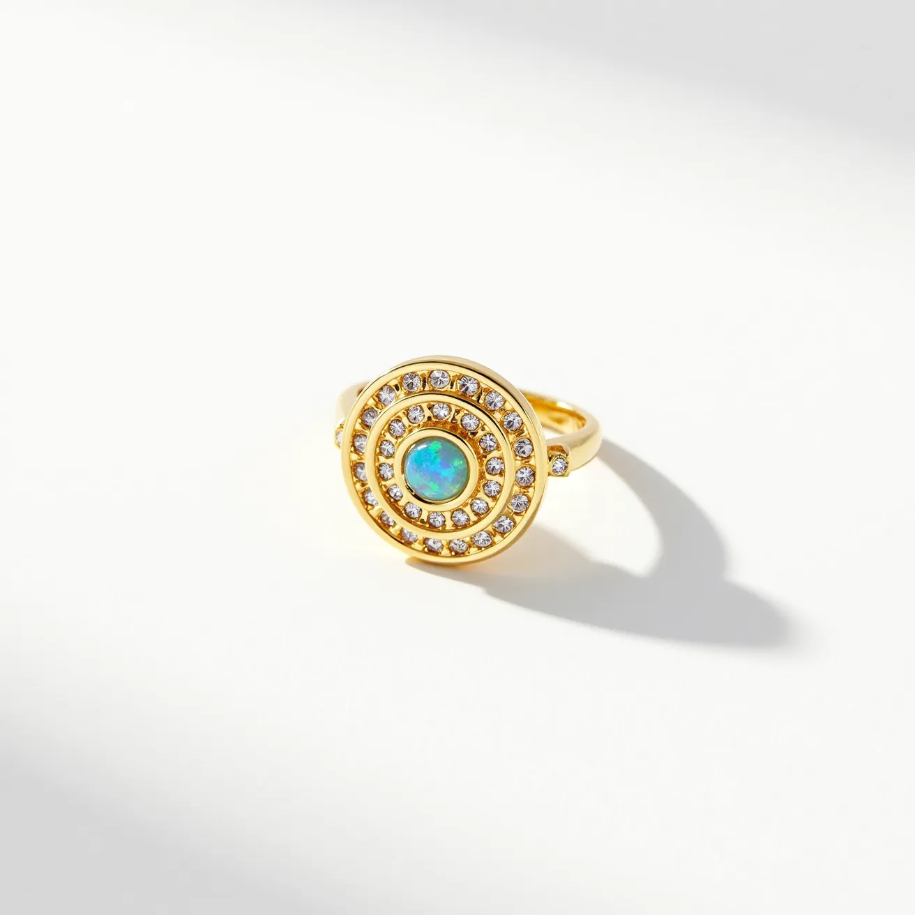 This cocktail ring features a striking design with a central opalescent stone as its focal point, displaying a mesmerizing play of colors typical of opals. The stone is cut in a round shape, enhancing its brilliance and depth. Surrounding the central stone are two concentric circles of smaller round-cut clear gemstones, likely diamonds or cubic zirconia, set in a pavé style that creates a glamorous effect. The setting and band are made of a polished yellow metal, possibly gold or gold-plated, providing a warm contrast to the cool hues of the opal. The ring does not feature any clasps or attachments, relying on the band for secure wear.