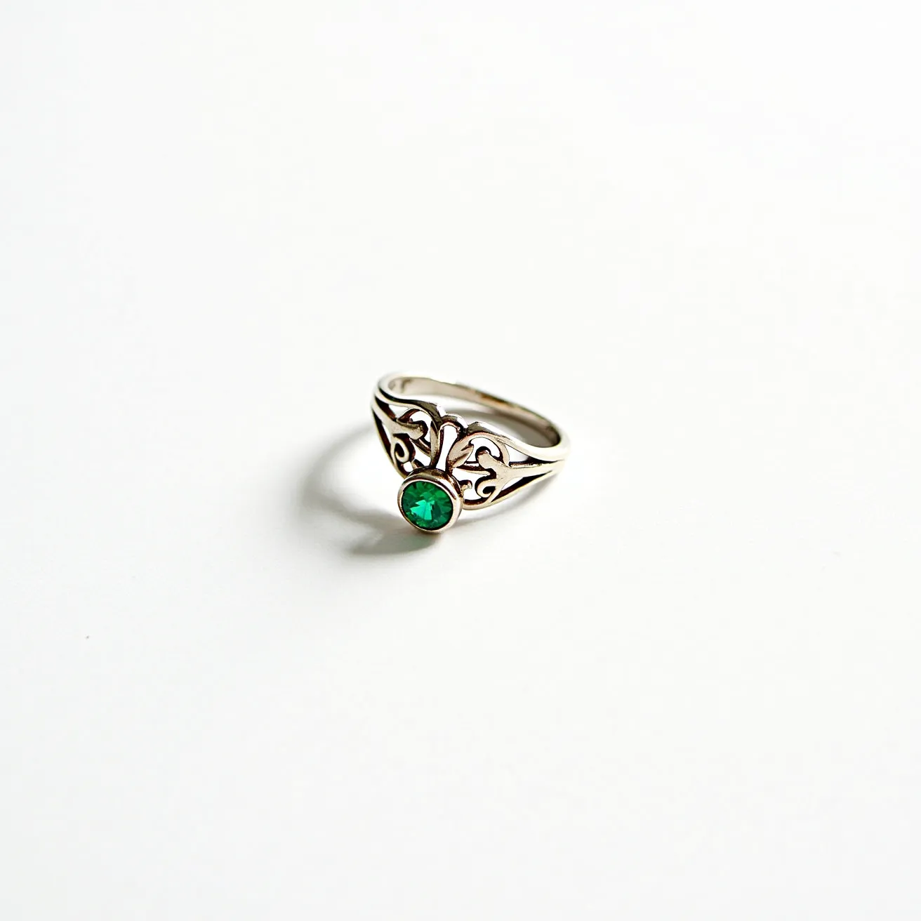 This cocktail ring showcases an intricate design featuring a vibrant green gemstone, likely an emerald, cut in a round shape. The stone is set in a secure bezel setting, allowing it to stand out prominently. The band is crafted from silver, possibly sterling, characterized by its elegant, swirling openwork filigree design, adding an artistic and vintage flair. The ring lacks any visible clasps or attachments, focusing solely on the intricate detailing and the central gemstone for its visual elegance.