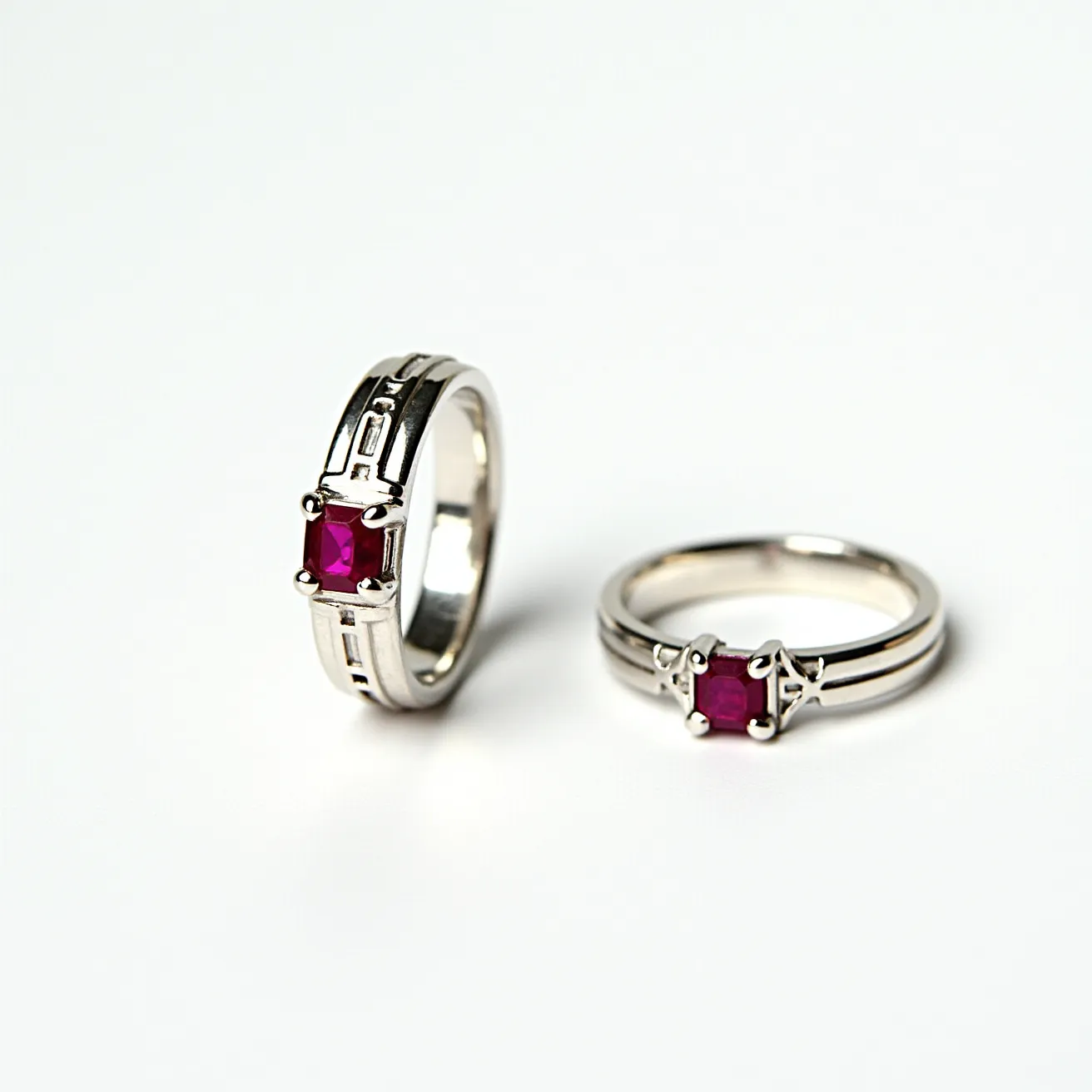 These couple rings appear to be crafted from a polished silver-toned metal and are designed as matching bands. Each ring features a prominent red gemstone, likely a ruby, which is square-cut to highlight its vibrant color. The gem is set in a secure, pronged setting that accentuates its symmetrical shape. The bands are adorned with subtle, engraved patterns that add a touch of elegance to the overall design. These rings do not have any visible clasps or attachments, focusing instead on the smooth, continuous metalwork.