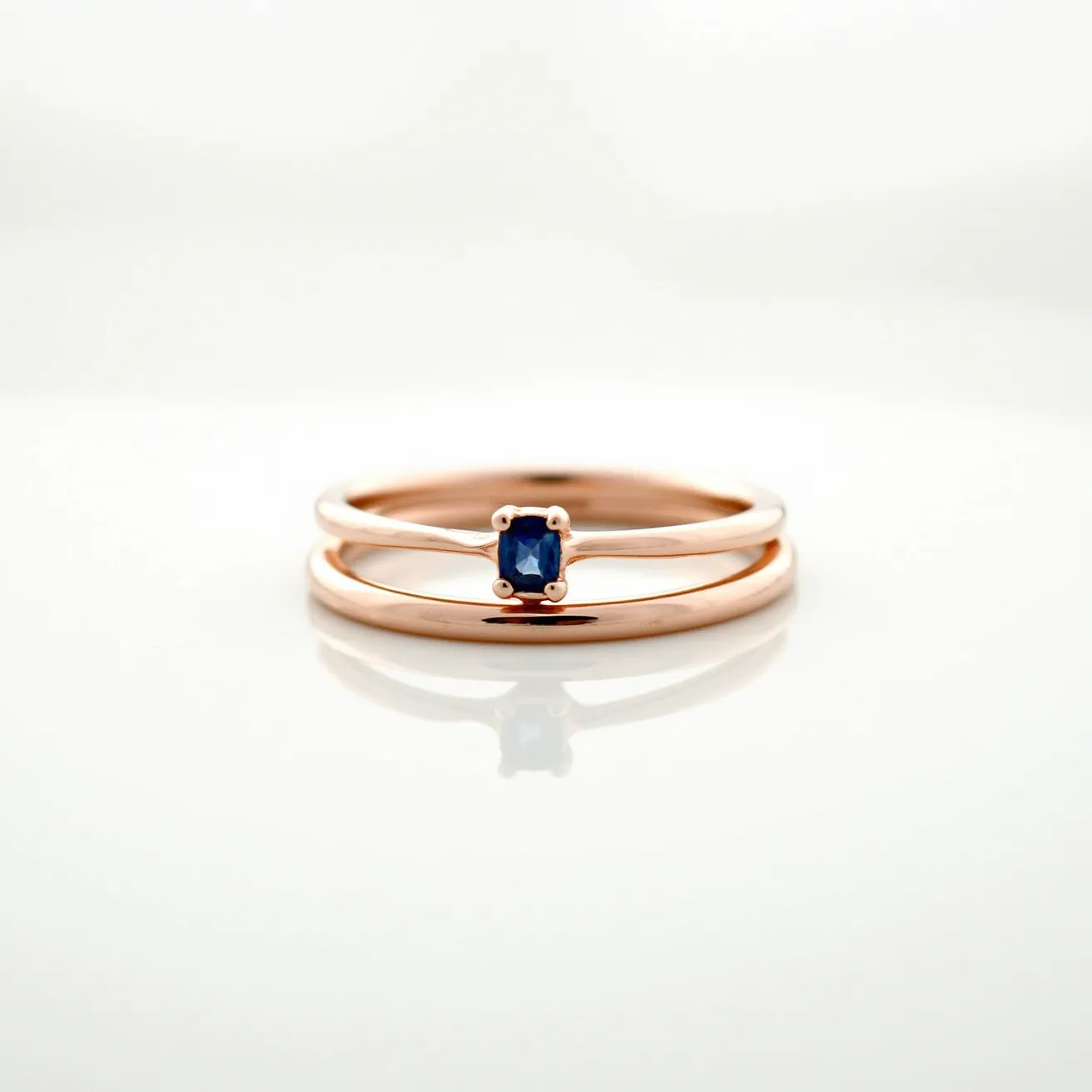 These couple rings feature two distinct bands with a minimalist design. The first band is crafted from white gold or platinum, offering a sleek and modern look, and is adorned with a small, deep blue sapphire. The sapphire is cut in a square shape and is held in place by four delicate prongs, giving it an elegant yet understated appearance. The second band is made of rose gold, which adds a warm and romantic contrast to the ensemble. The simplicity and elegance of these rings make them a perfect symbol of unity and commitment.