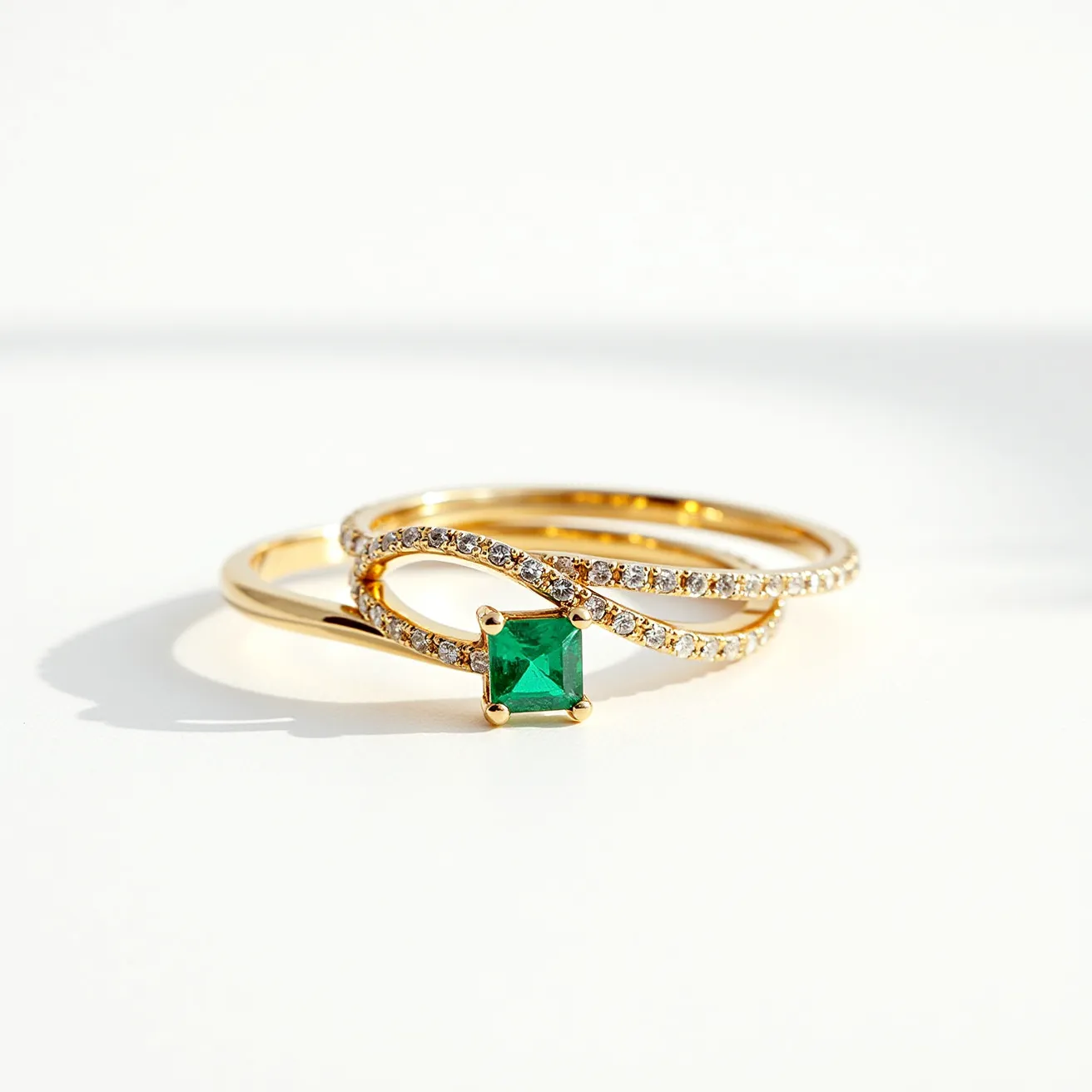 These couple rings feature an elegant design crafted from gold. One ring showcases a prominent square-cut emerald set in a four-prong setting, adding a vibrant green focal point. The other ring is adorned with small round brilliant-cut diamonds, which are pave-set to form a graceful interwoven pattern that complements the emerald ring beautifully. The two rings are designed to be worn together, offering a harmonious blend of color and sparkle.