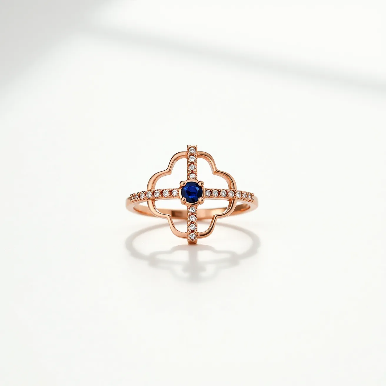 This cross ring features a sophisticated design crafted from rose gold. At its center, it showcases a round-cut blue gemstone, likely a sapphire, held in a prong setting. The ring's band and cross motif are adorned with a series of small, sparkling white stones set in a micro-pavé style, adding elegance and brilliance. The overall aesthetic is one of delicate symmetry, with the materials and setting creating a harmonious balance.